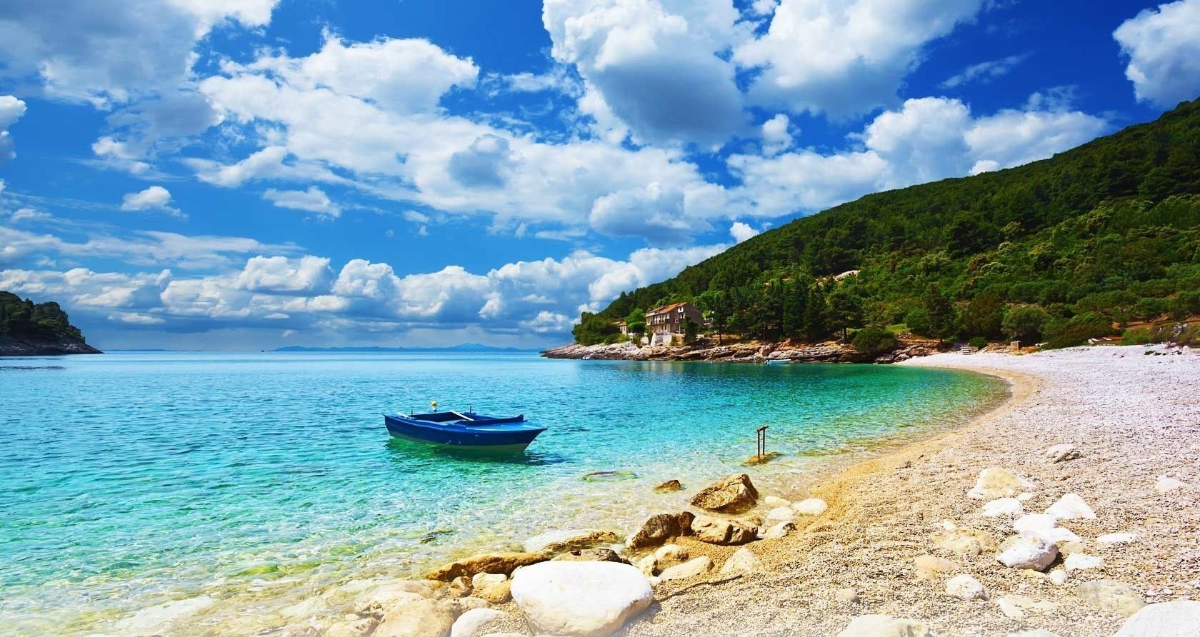 A secluded cove with a blue boat and a house on the hill HD Wallpaper