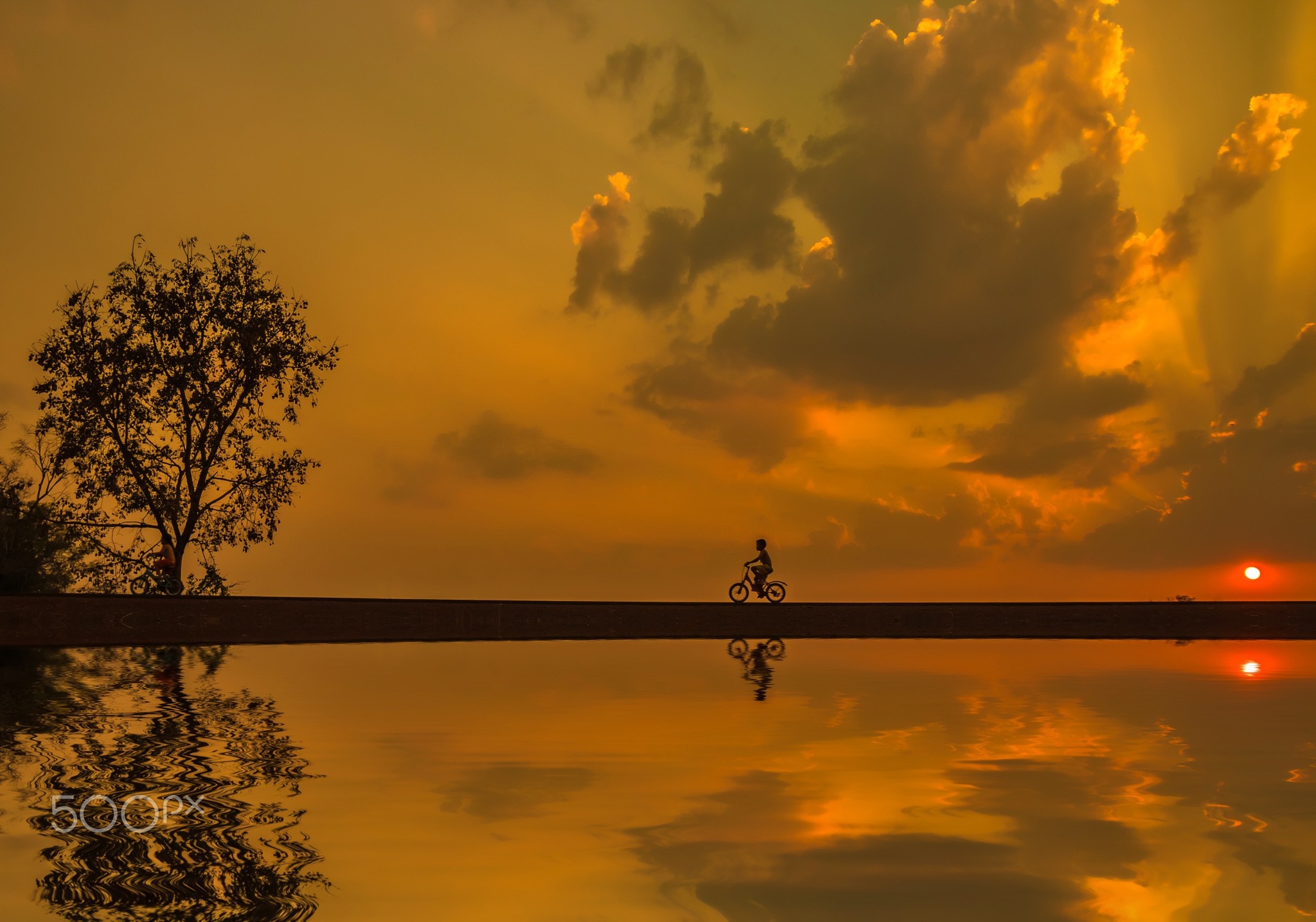 Silhouette of a child on a bicycle at sunset reflected in water HD Wallpaper