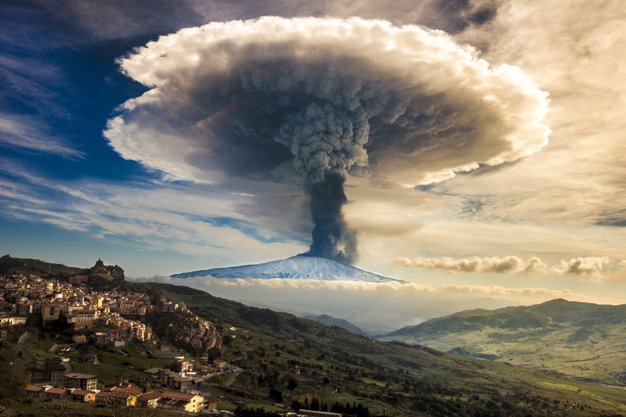 Volcano erupting with ash cloud over a town and mountains HD Wallpaper