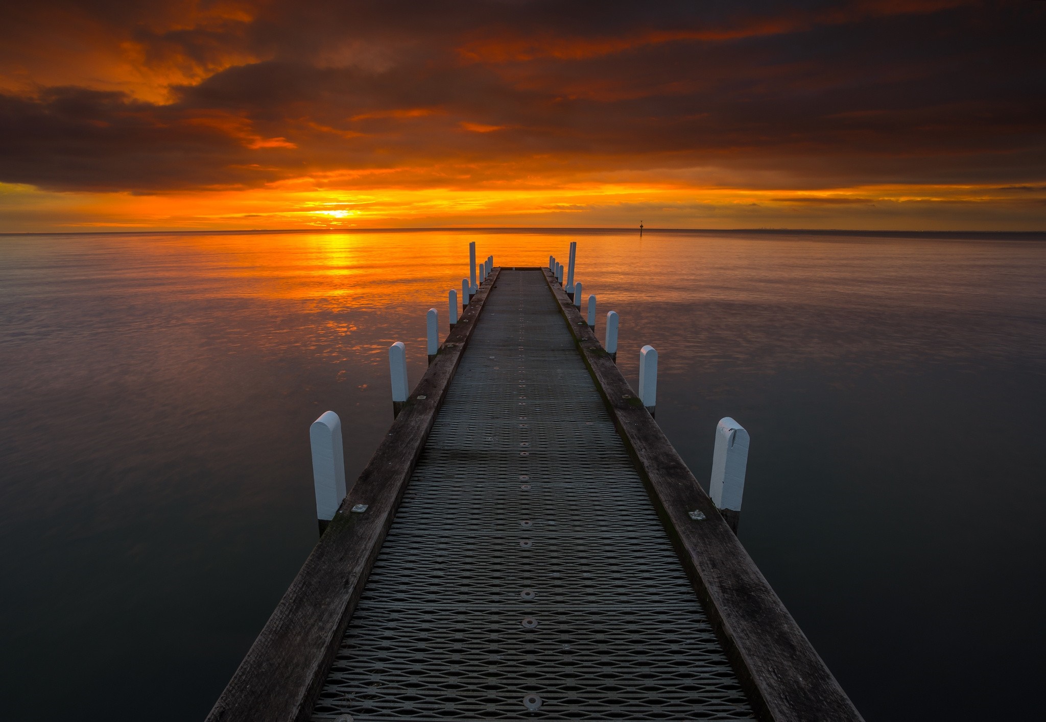 Pier extending into the ocean at sunset HD Wallpaper