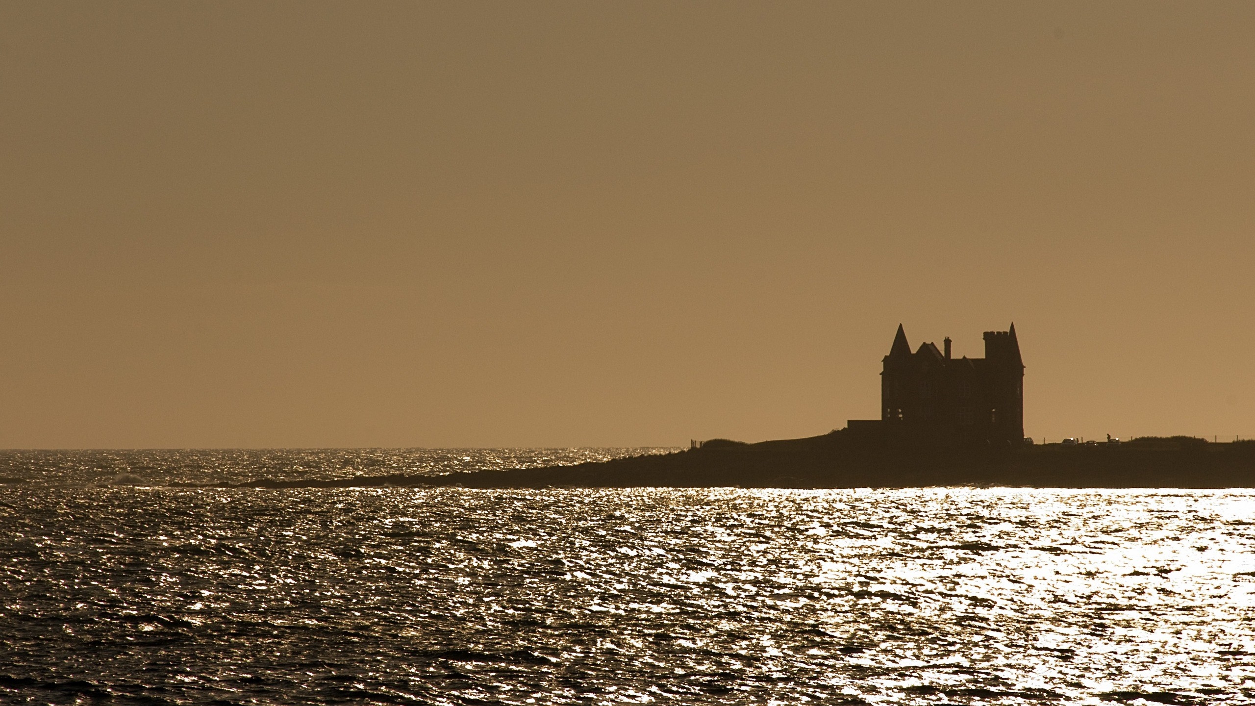 Silhouette of a castle on a rocky shore at sunset HD Wallpaper