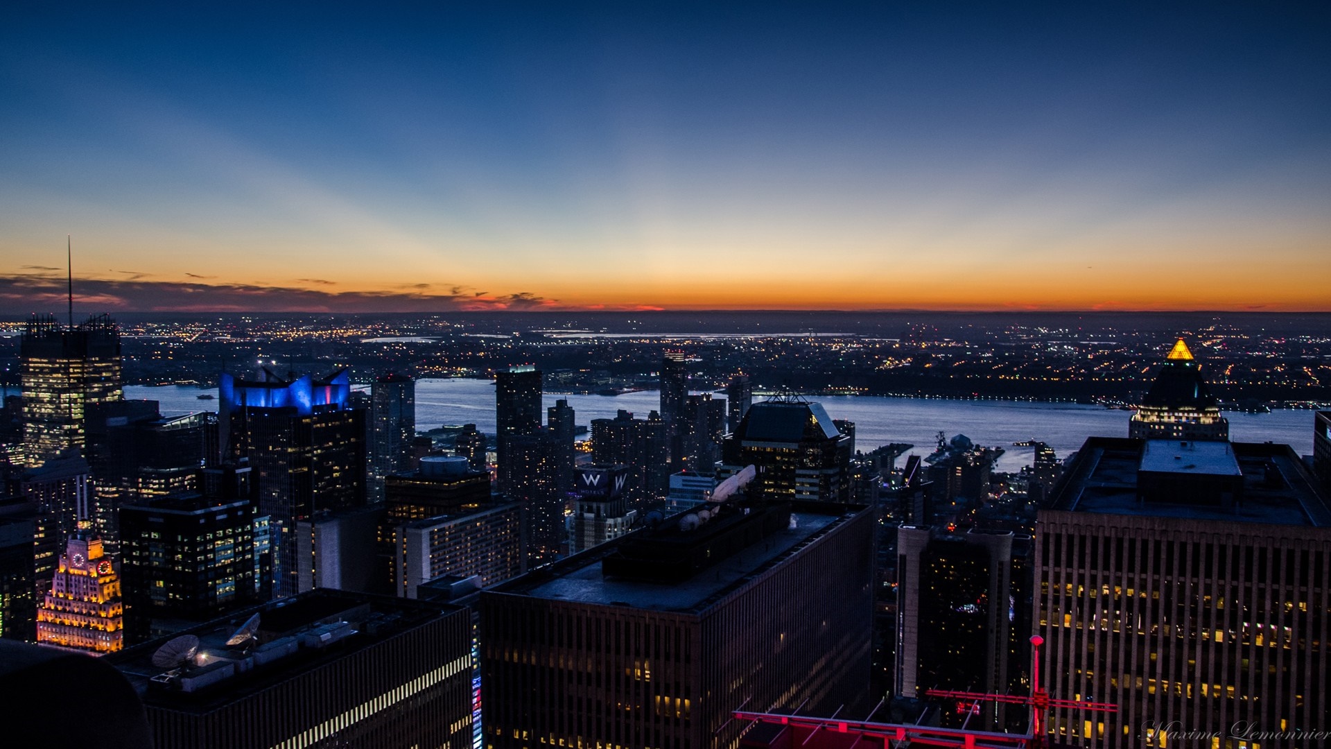 Cityscape at dusk with river and illuminated skyscrapers HD Wallpaper