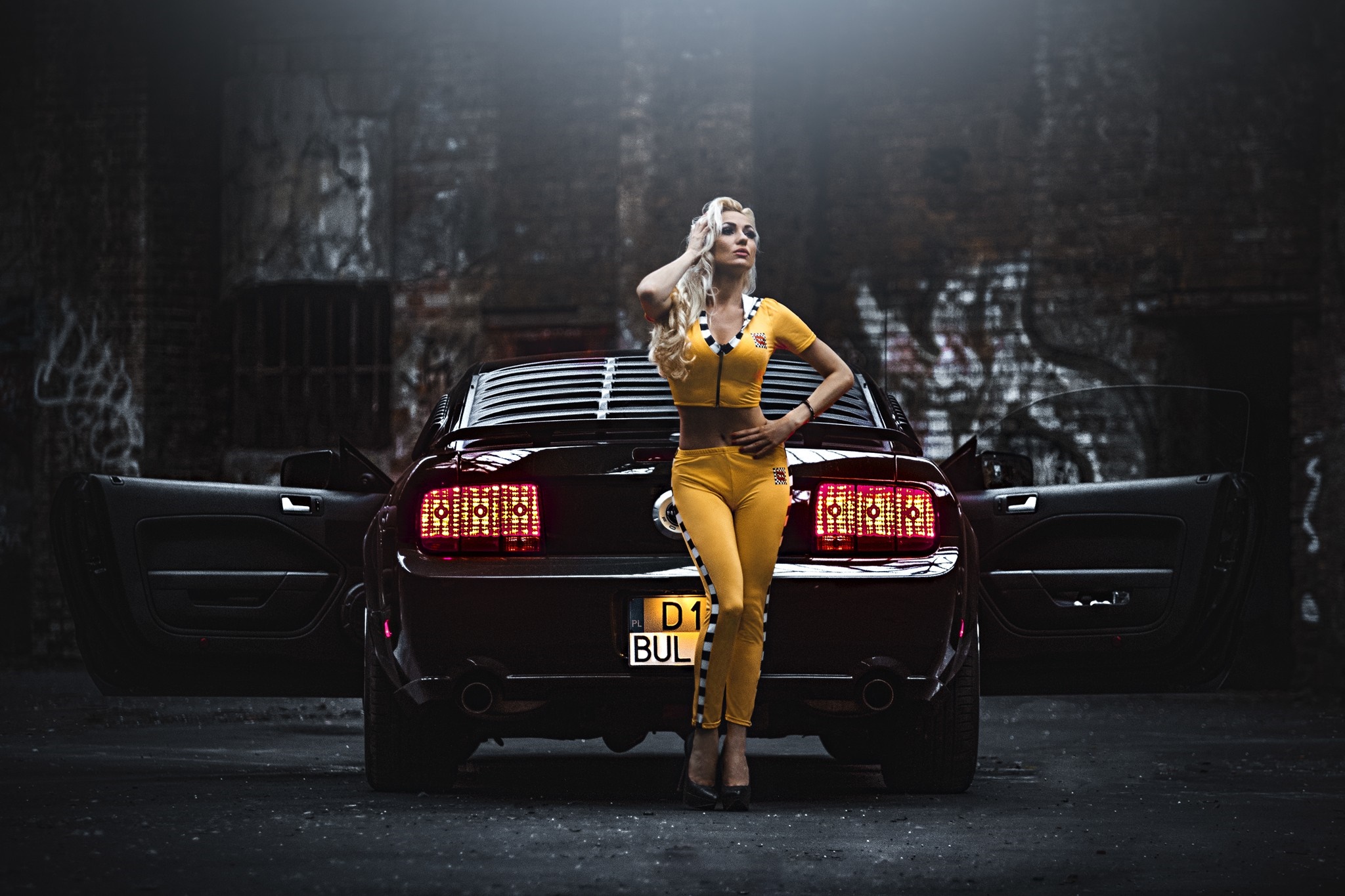 Woman in yellow racing suit posing with a red Ford Mustang HD Wallpaper