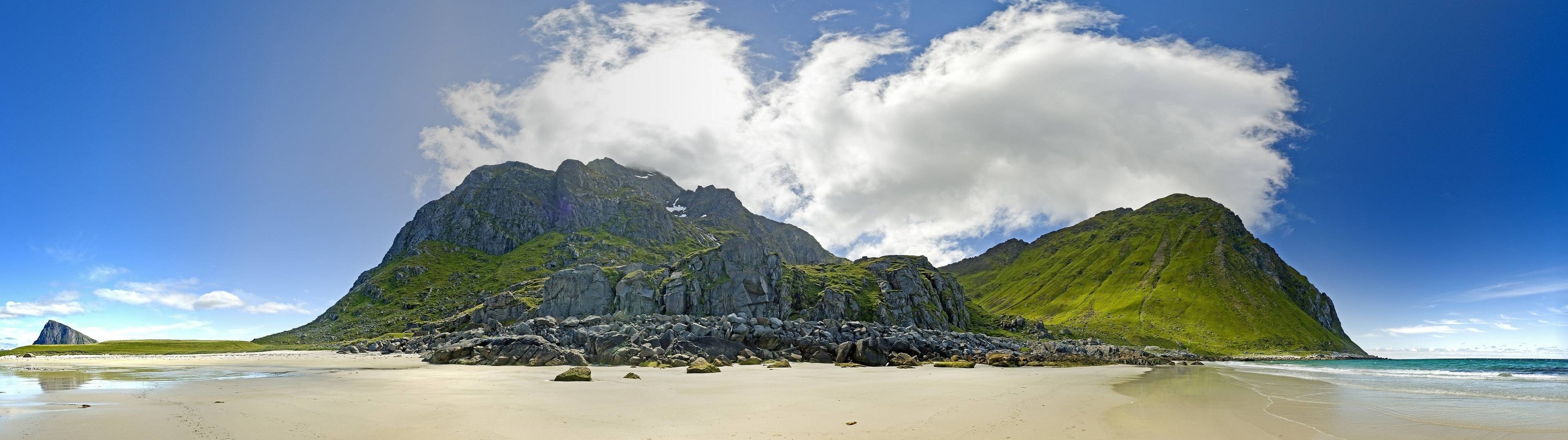 Panoramic view of a rocky coastline with green mountains and a sandy beach HD Wallpaper
