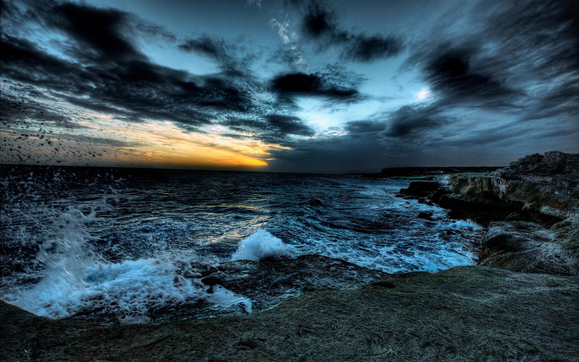 Stormy ocean waves crash against rocky cliffs at sunset HD Wallpaper