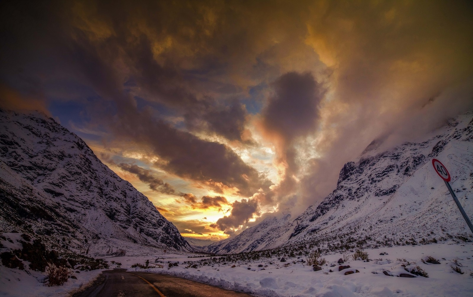 Snowy mountain pass at sunset with a road HD Wallpaper