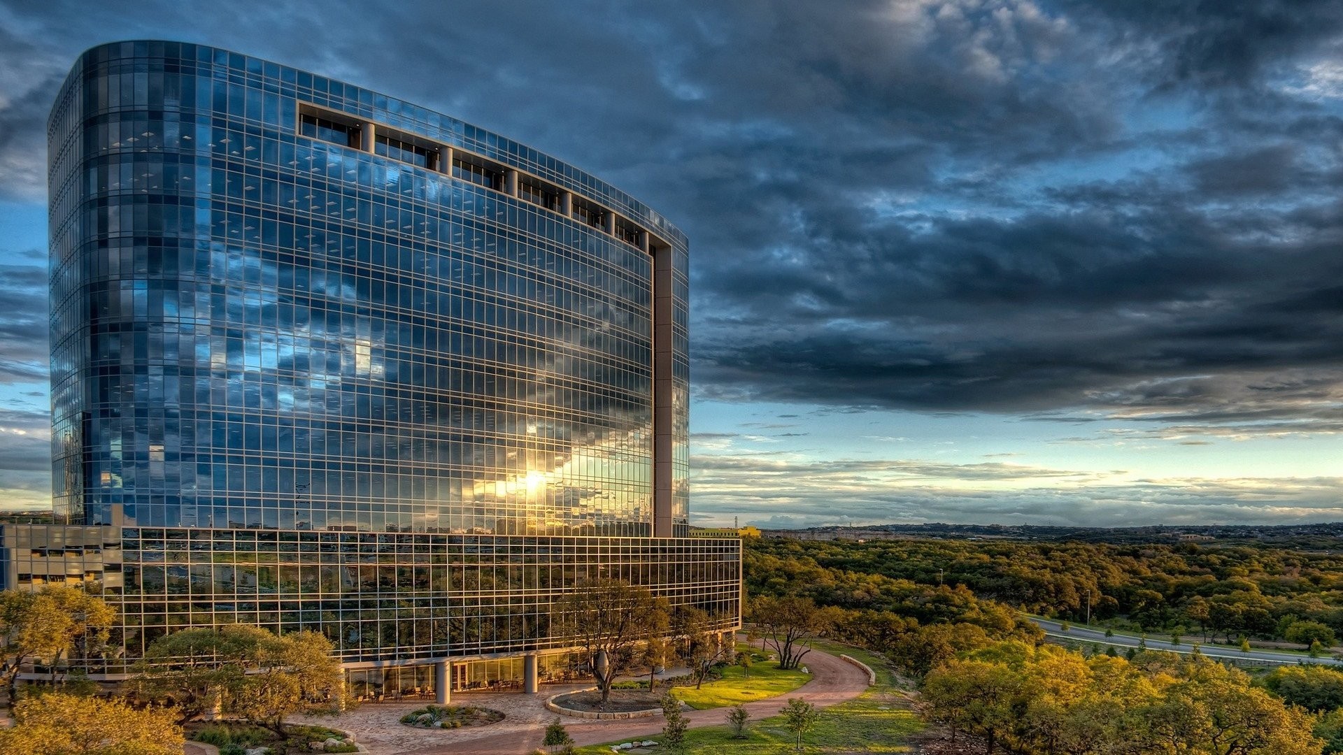 Modern glass office building at sunset with dramatic clouds HD Wallpaper