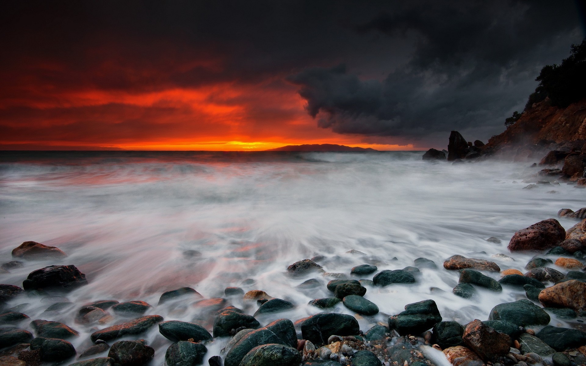Dramatic sunset over a rocky shore with crashing waves HD Wallpaper