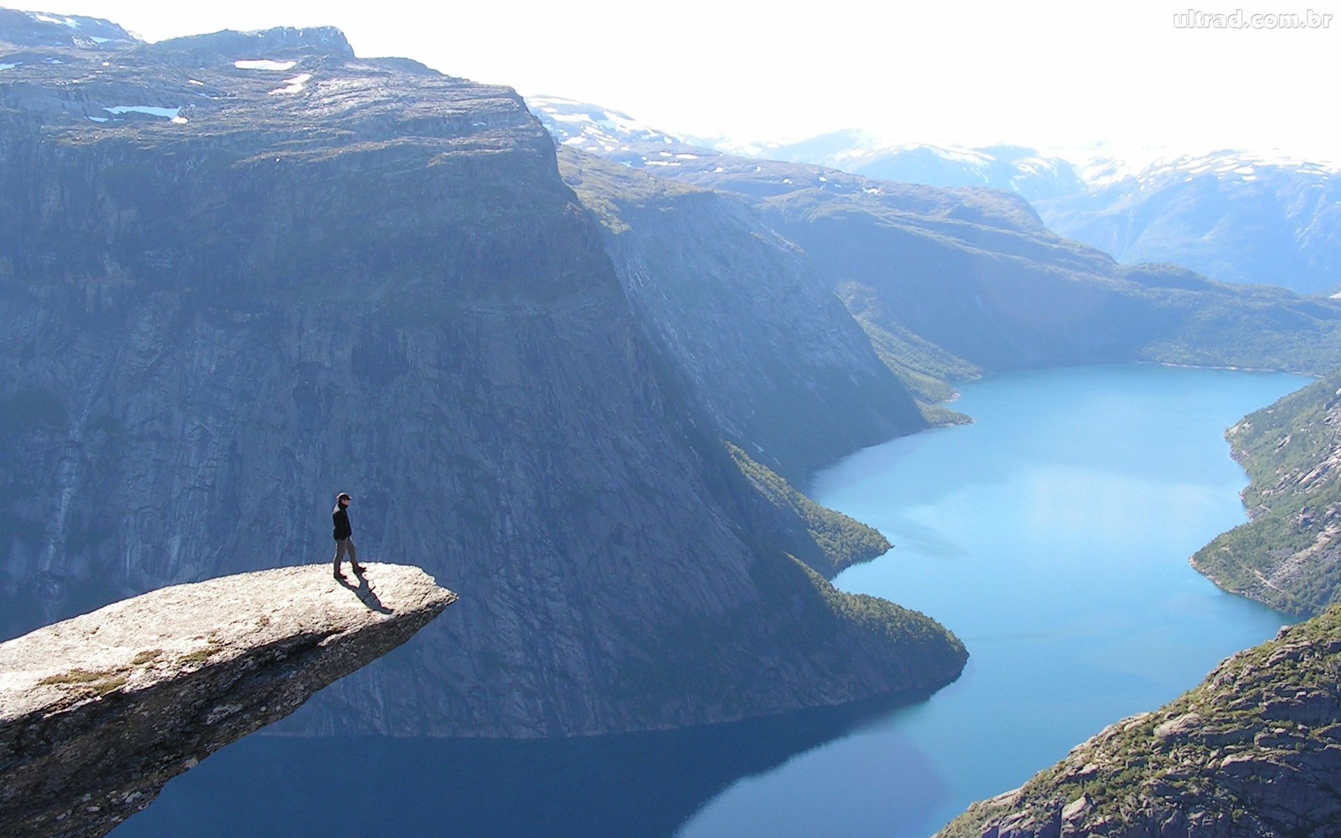 Person standing on Trolltunga cliff overlooking a fjord in Norway HD Wallpaper