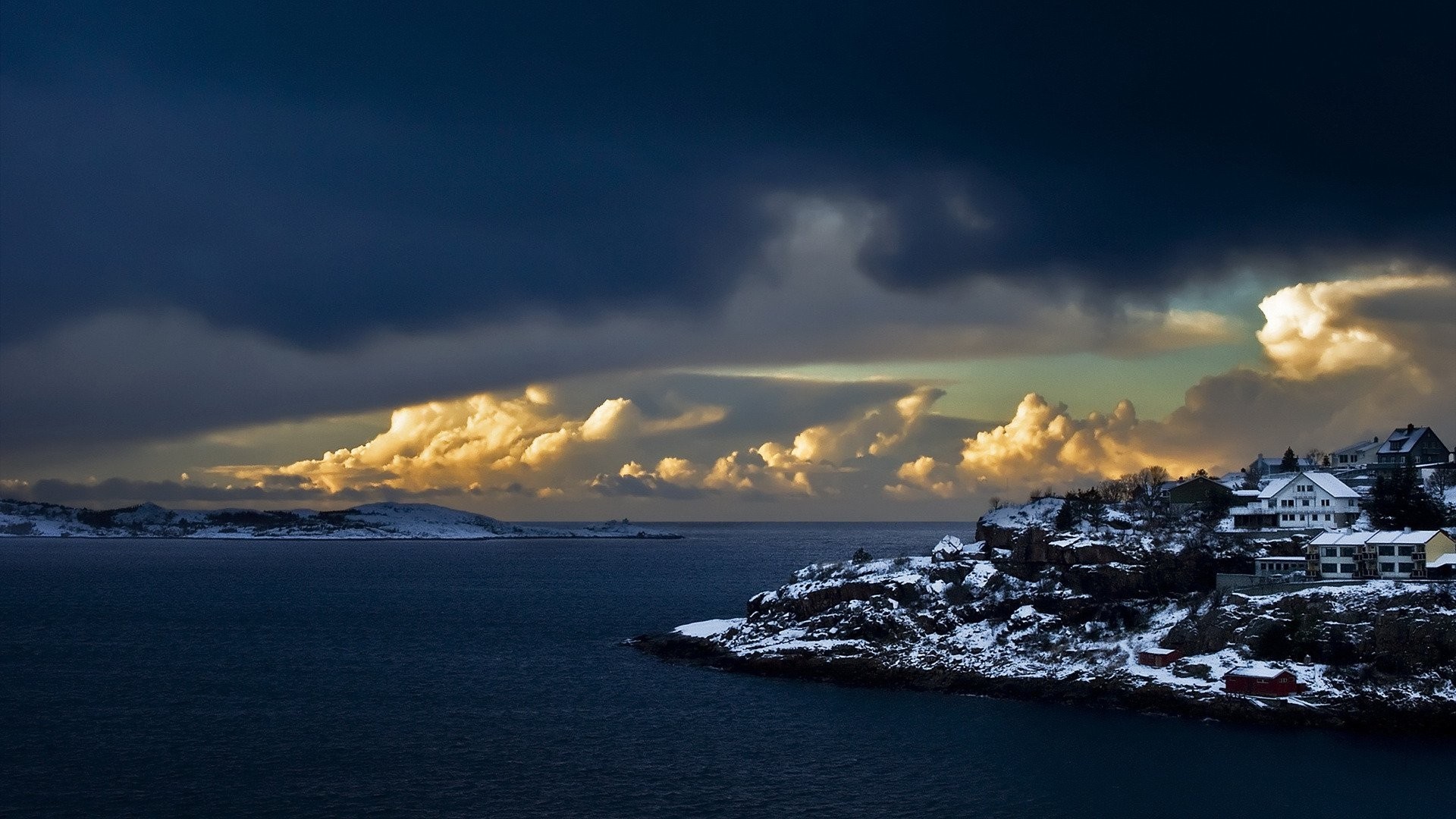 Snowy coastal village under dramatic clouds HD Wallpaper