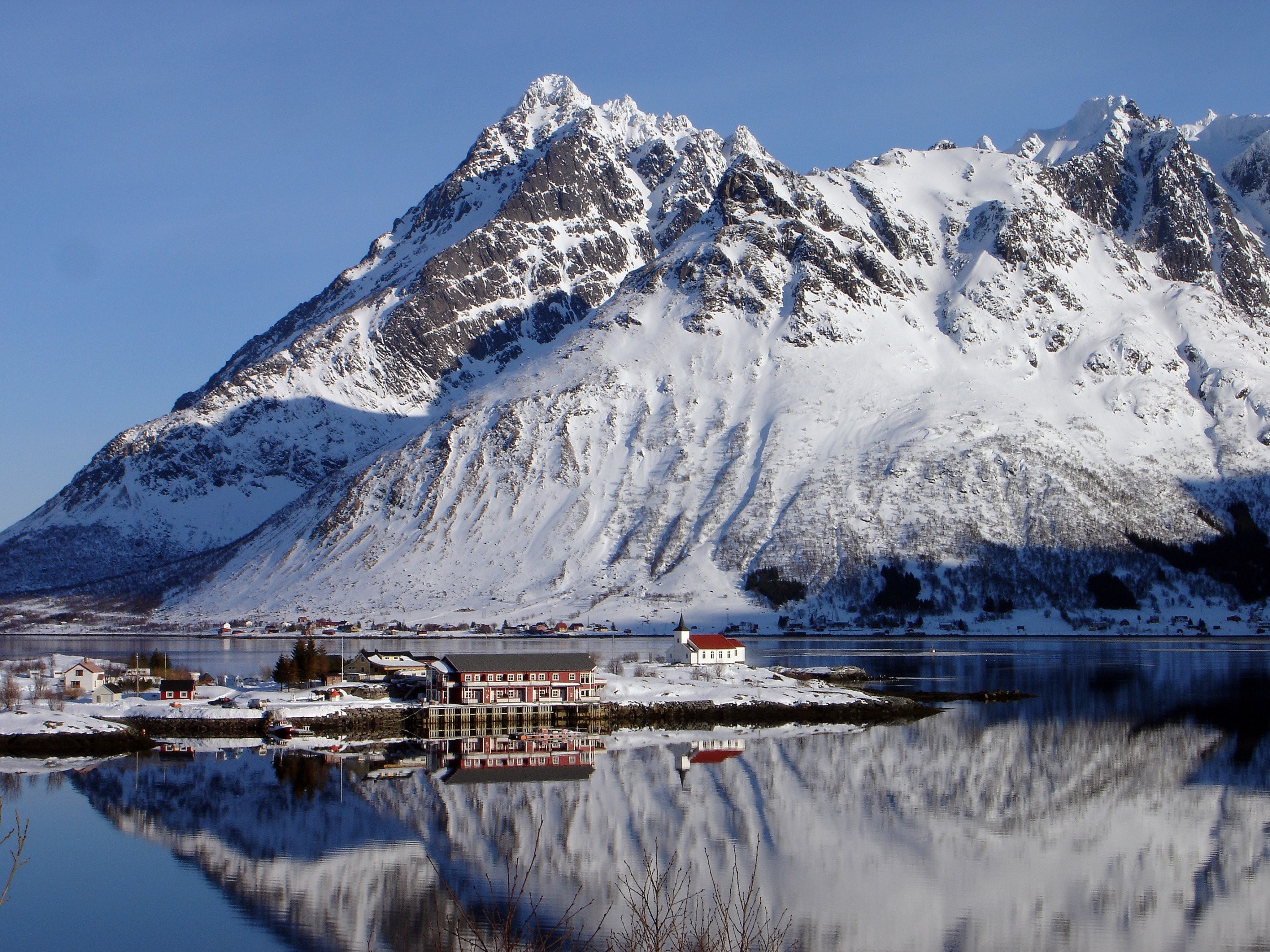 Snowy mountains reflected in a calm lake with a village HD Wallpaper