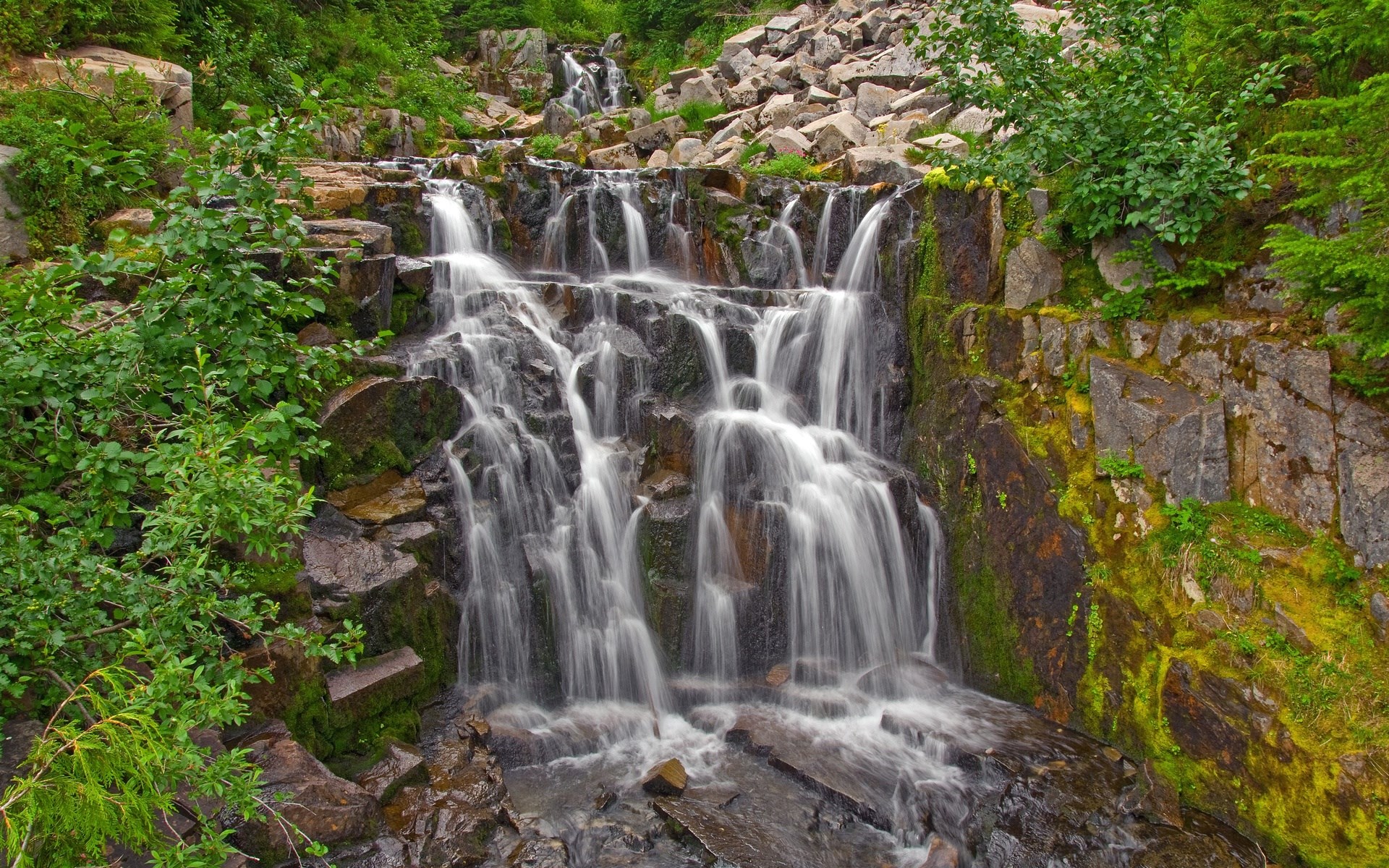 Waterfall cascading over rocks with green foliage HD Wallpaper