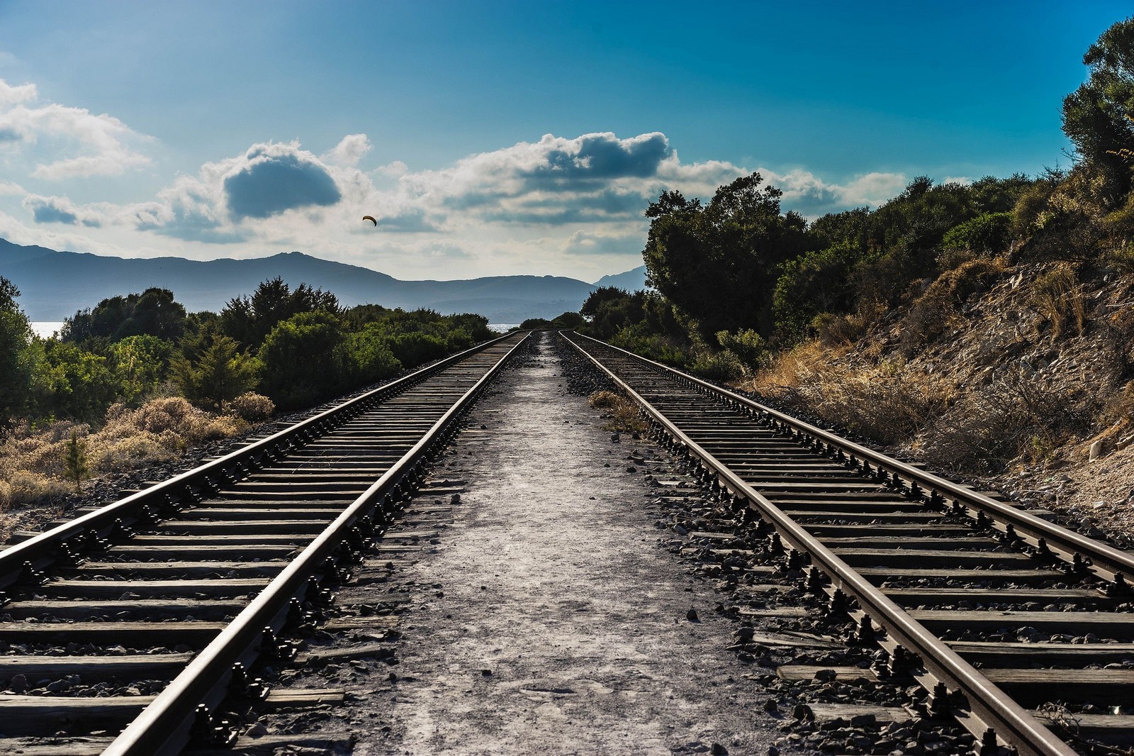 Railroad tracks leading to mountains under a blue sky HD Wallpaper