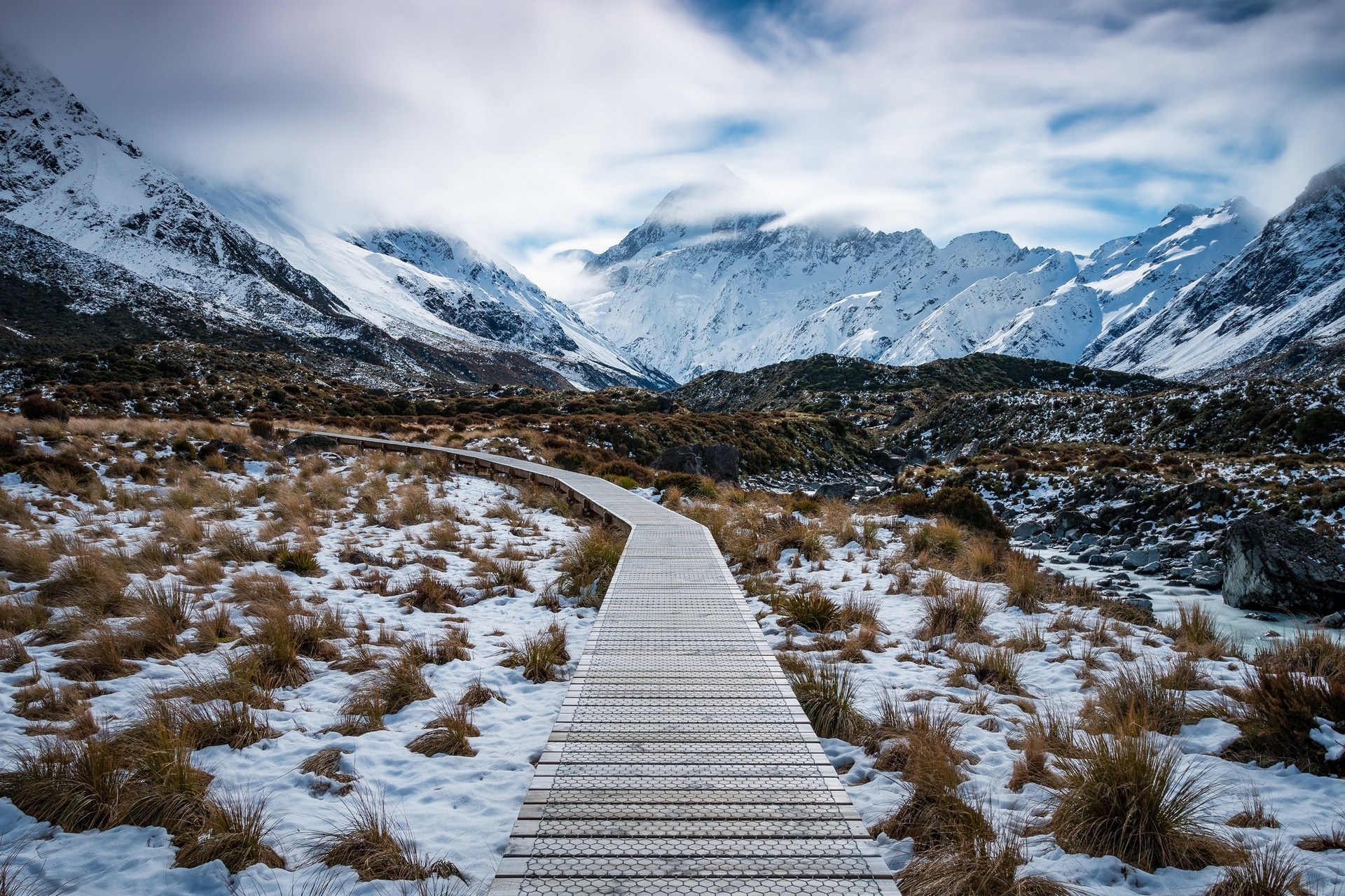 Wooden boardwalk through snowy mountains and dry grass HD Wallpaper
