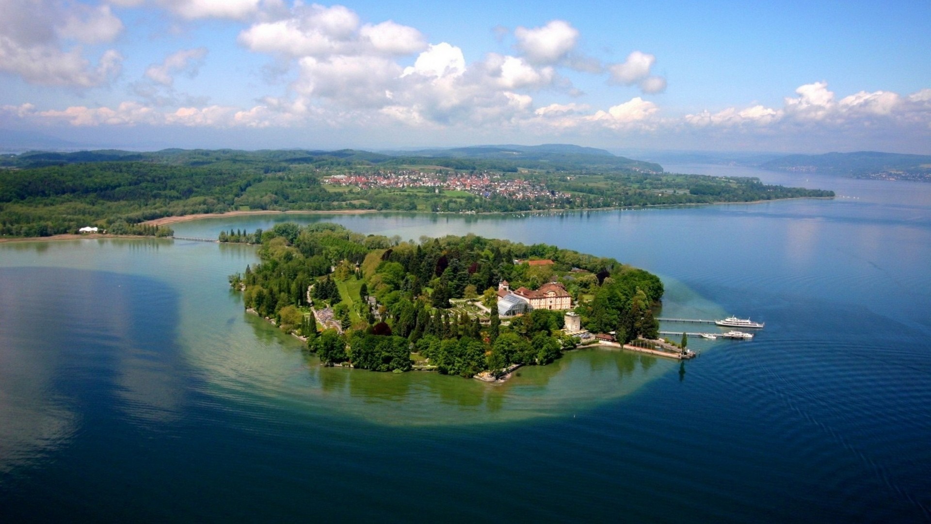 Island with buildings on a lake with a town in the background HD Wallpaper