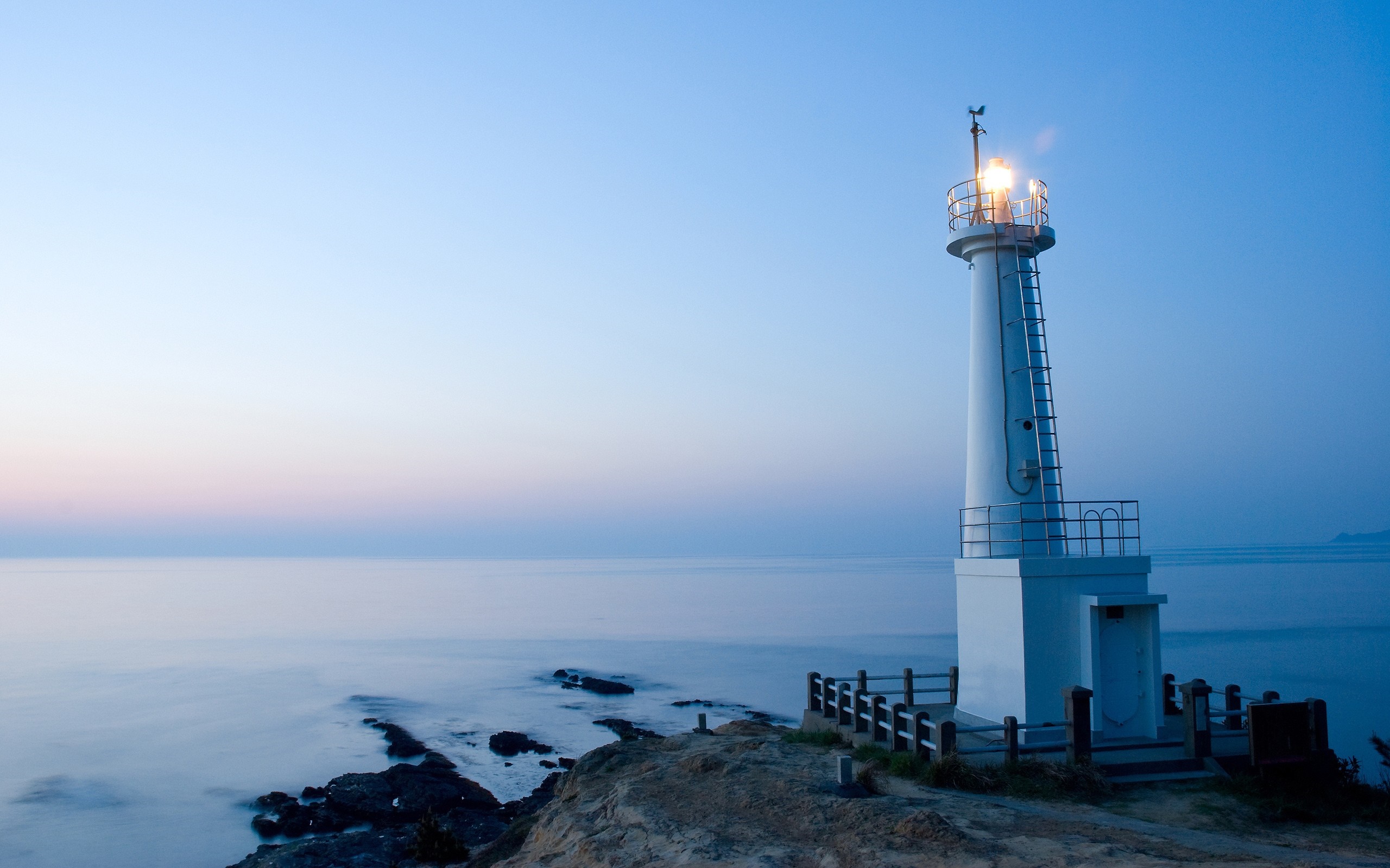 White lighthouse on a rocky coast at dusk HD Wallpaper