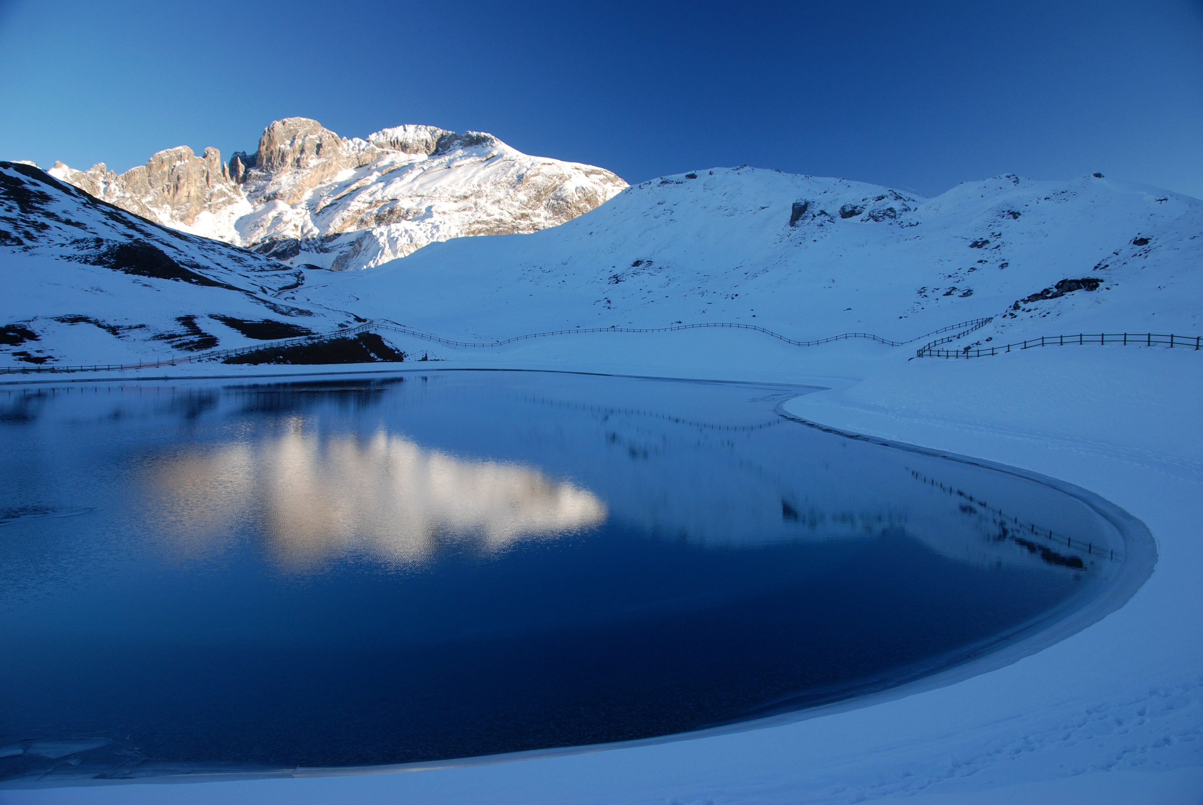 Snowy mountains reflected in a calm lake under a clear blue sky HD Wallpaper
