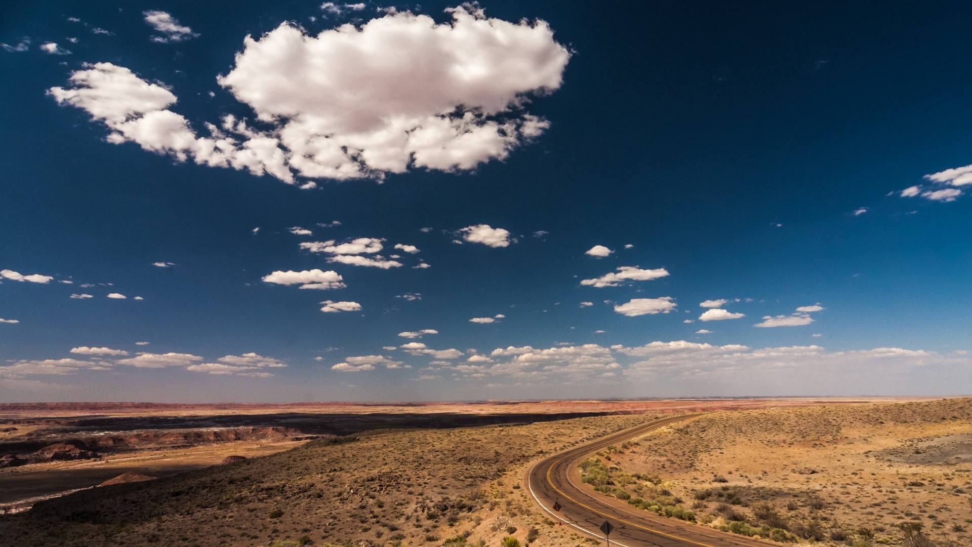 Desert landscape with a winding road under a cloudy blue sky HD Wallpaper