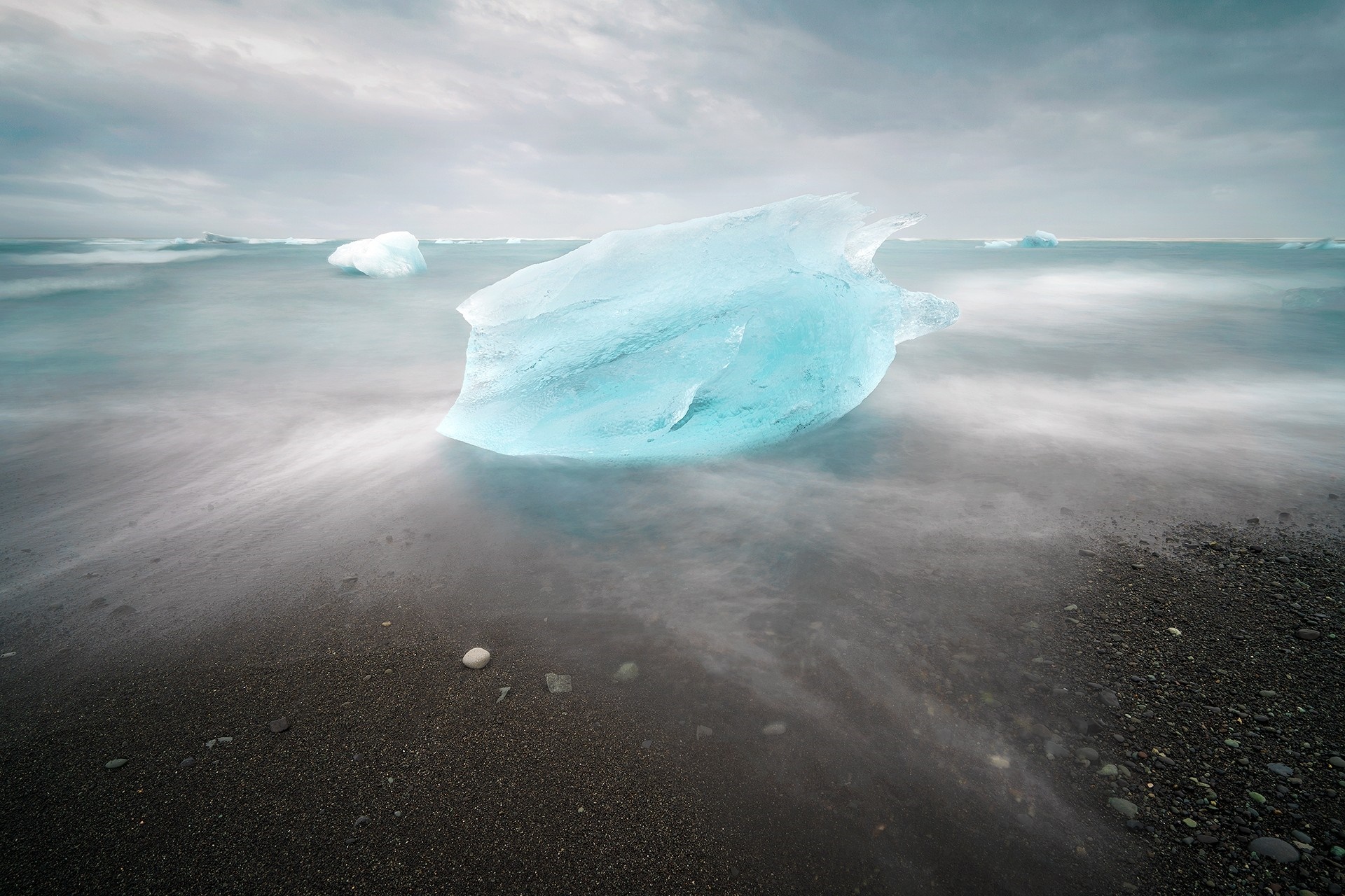 Iceberg on a black sand beach with ocean waves HD Wallpaper