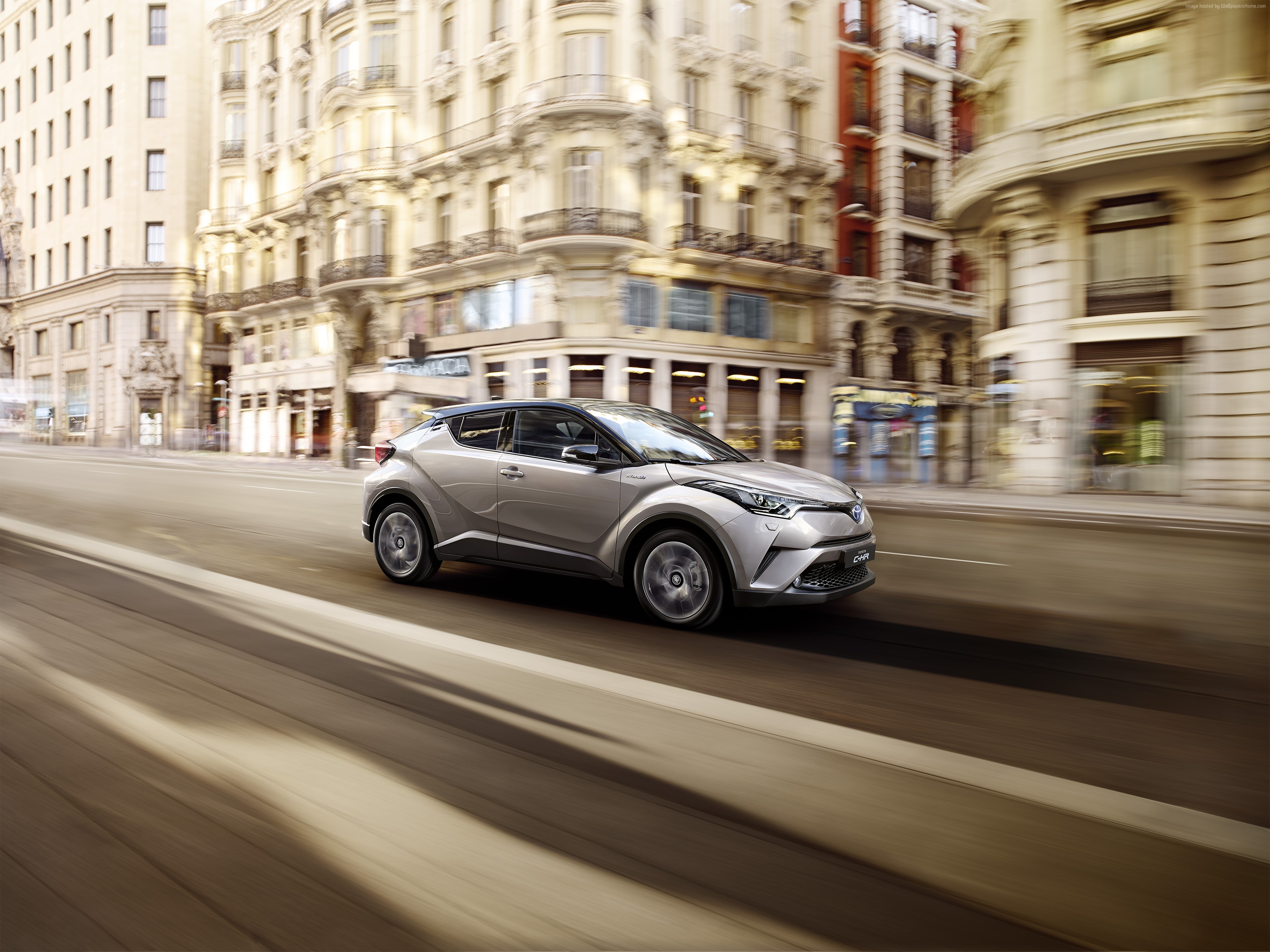 Silver Toyota C-HR driving on a city street HD Wallpaper