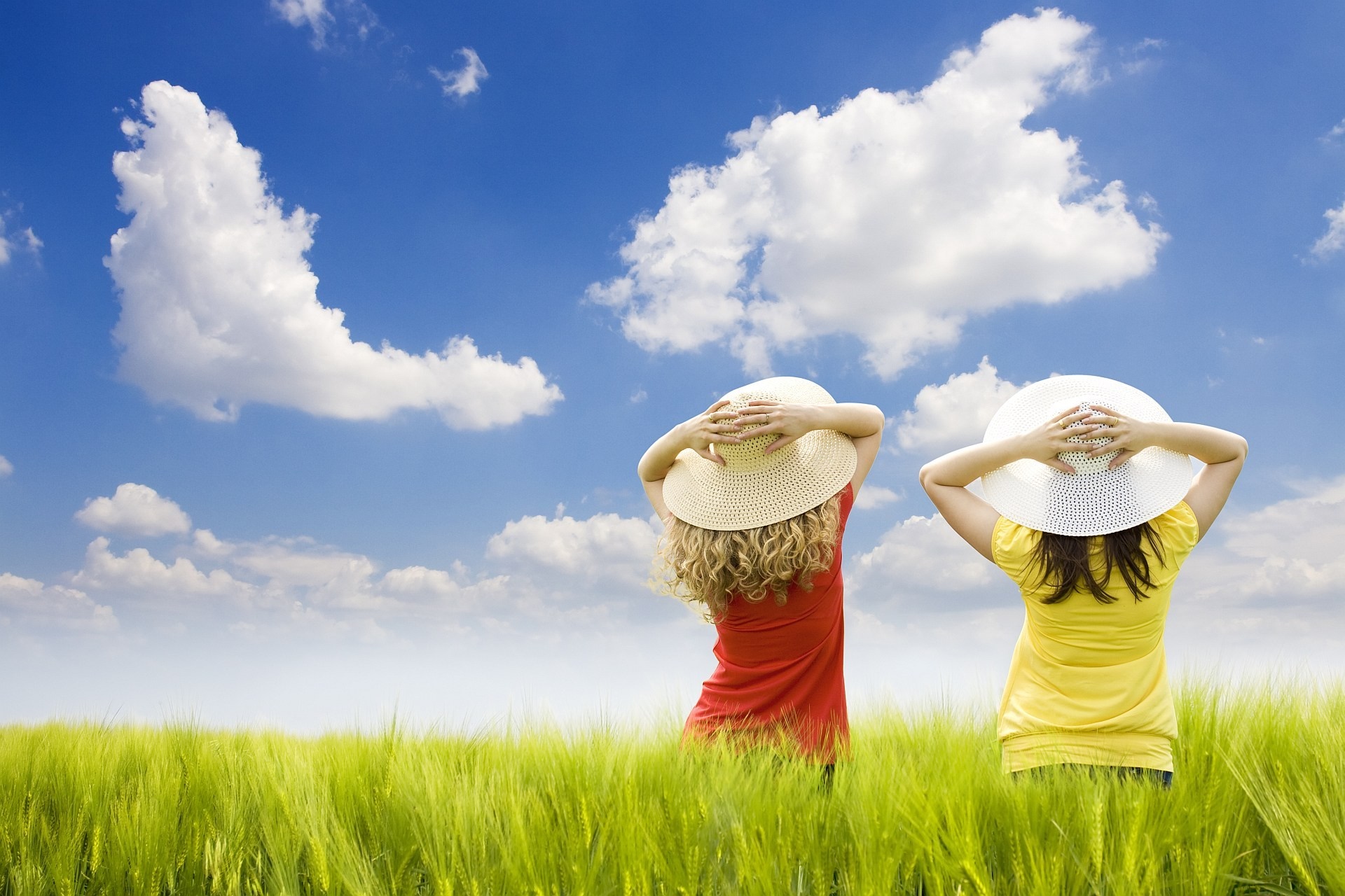 Two girls in hats in a green field under the sky HD Wallpaper