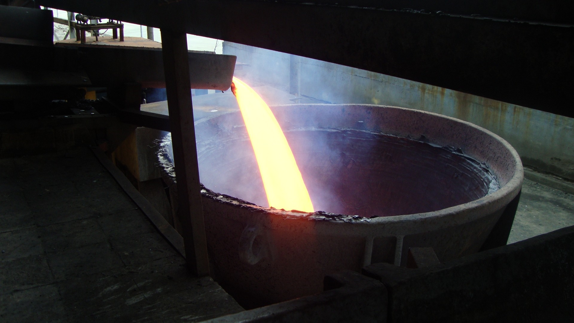Molten metal being poured into a large industrial vat HD Wallpaper