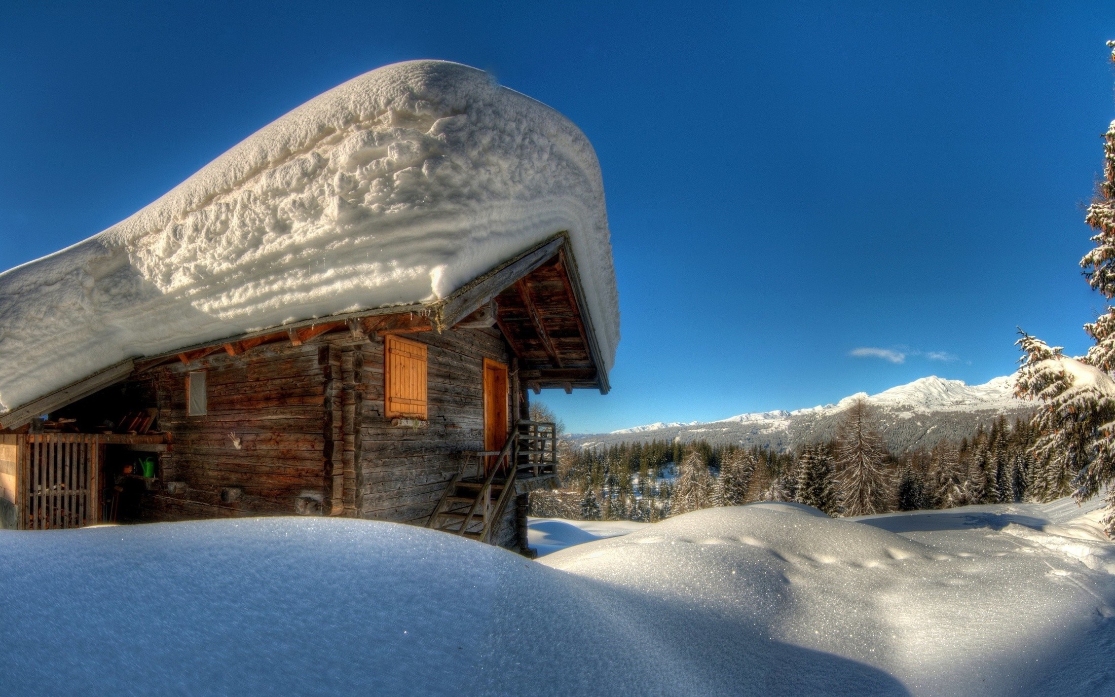 Wooden hut covered in snow with mountains in the background HD Wallpaper