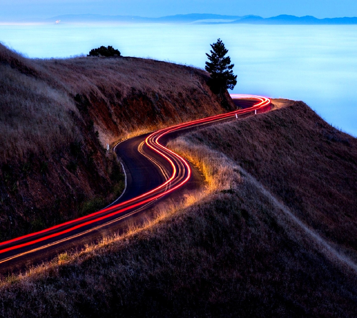 Winding road with light trails on a hill at dusk HD Wallpaper