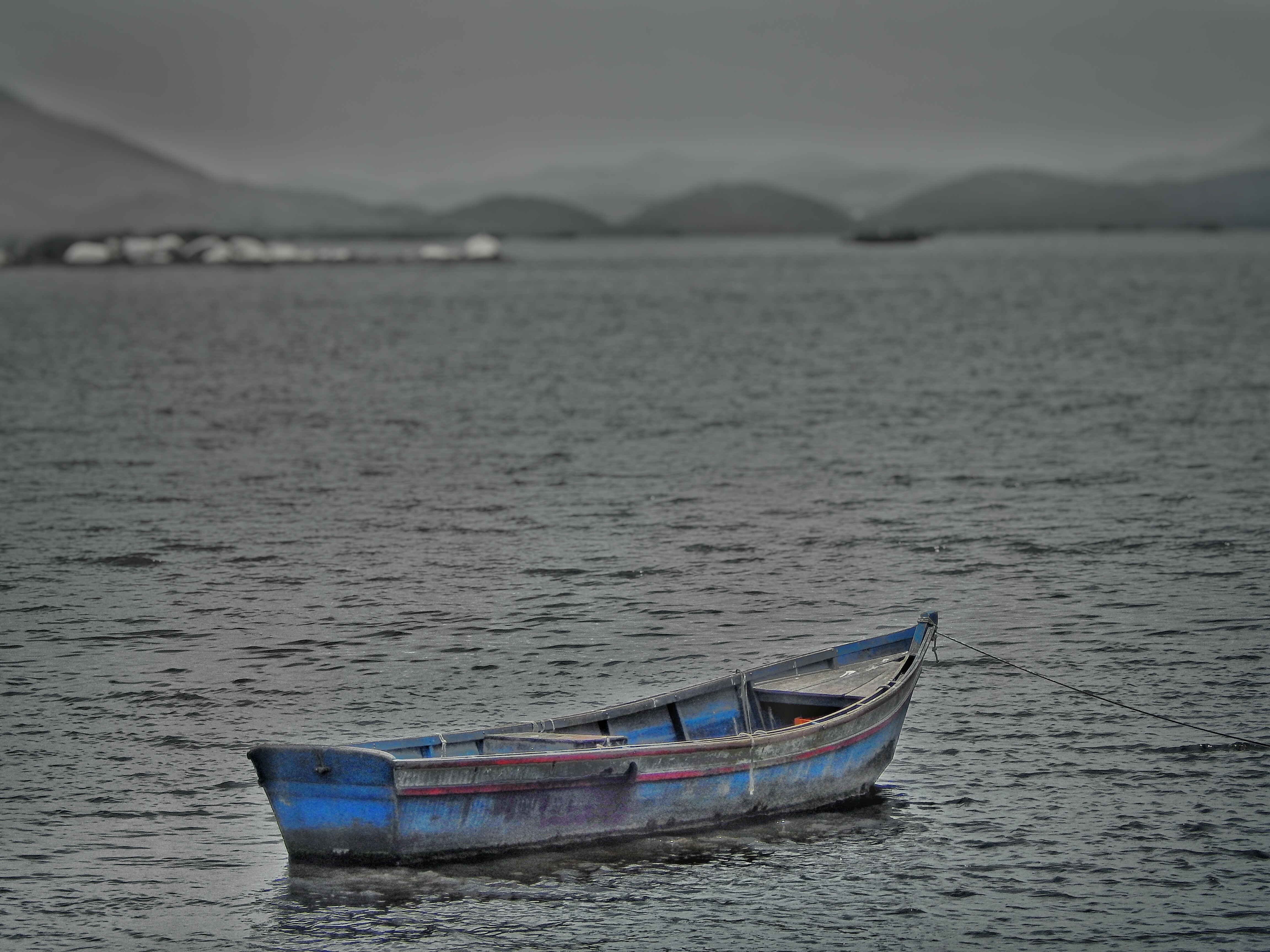 A blue boat floats on the water near a distant shore. HD Wallpaper