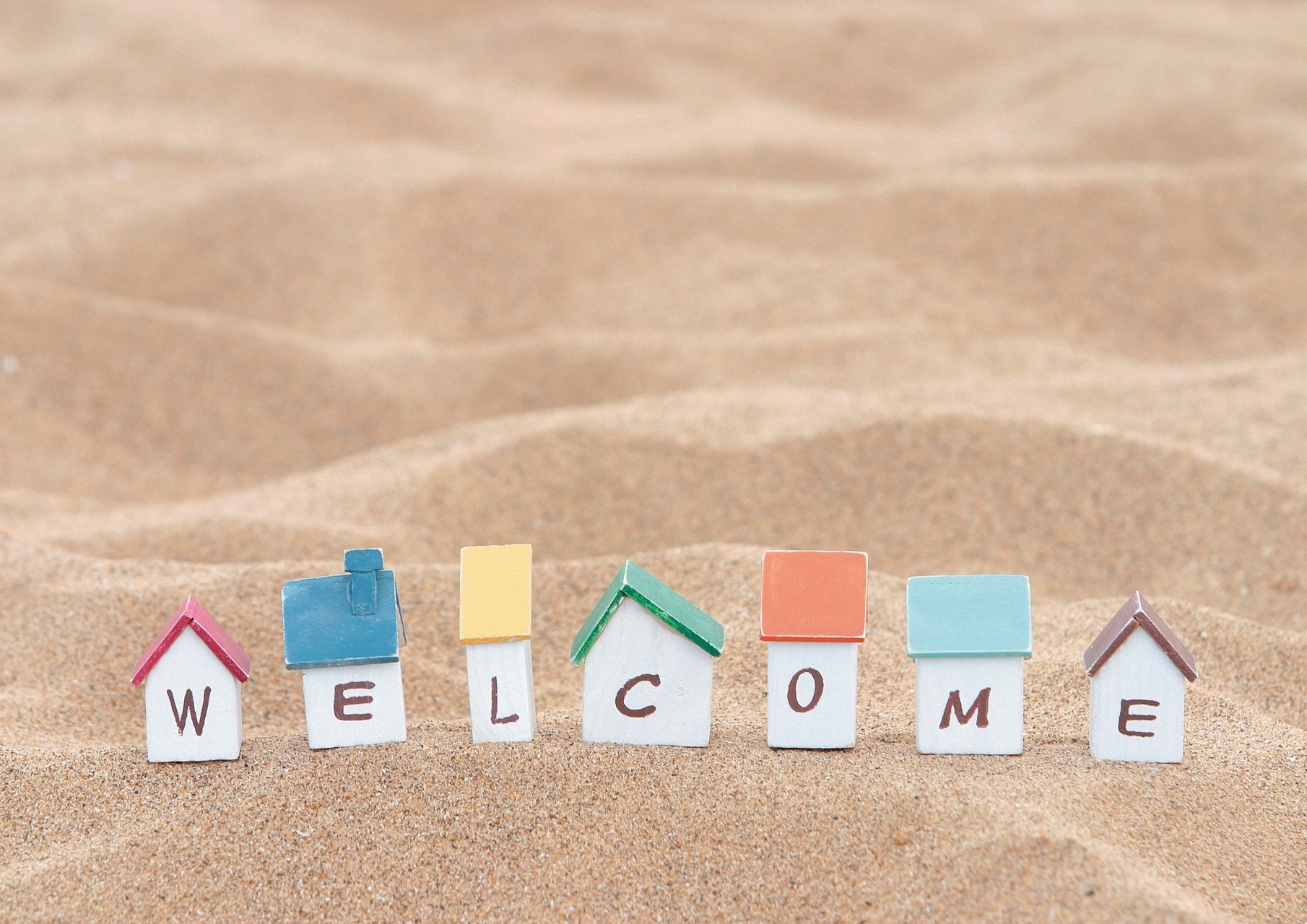 Miniature houses spelling WELCOME on sand HD Wallpaper
