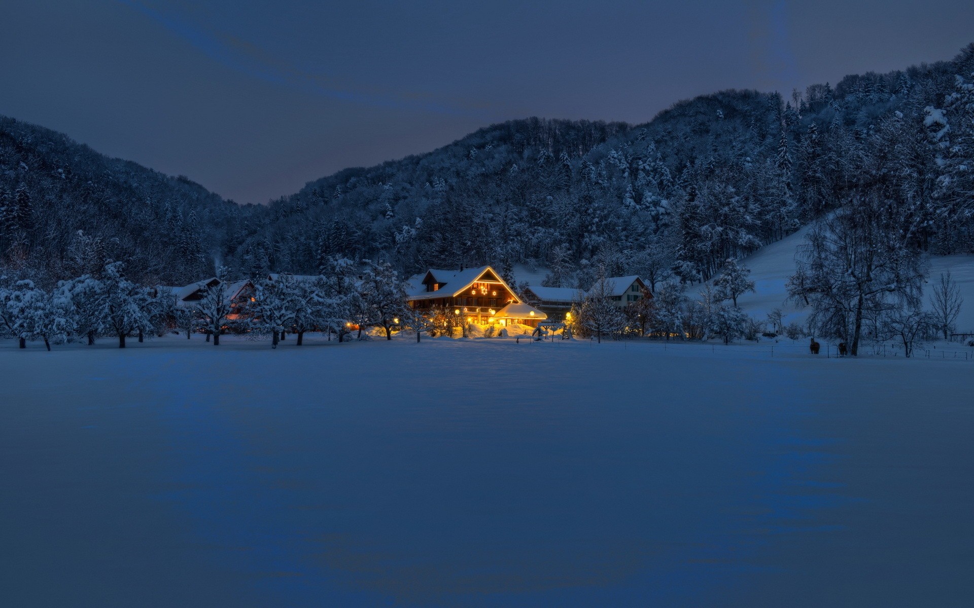 Snowy village with illuminated houses at dusk HD Wallpaper