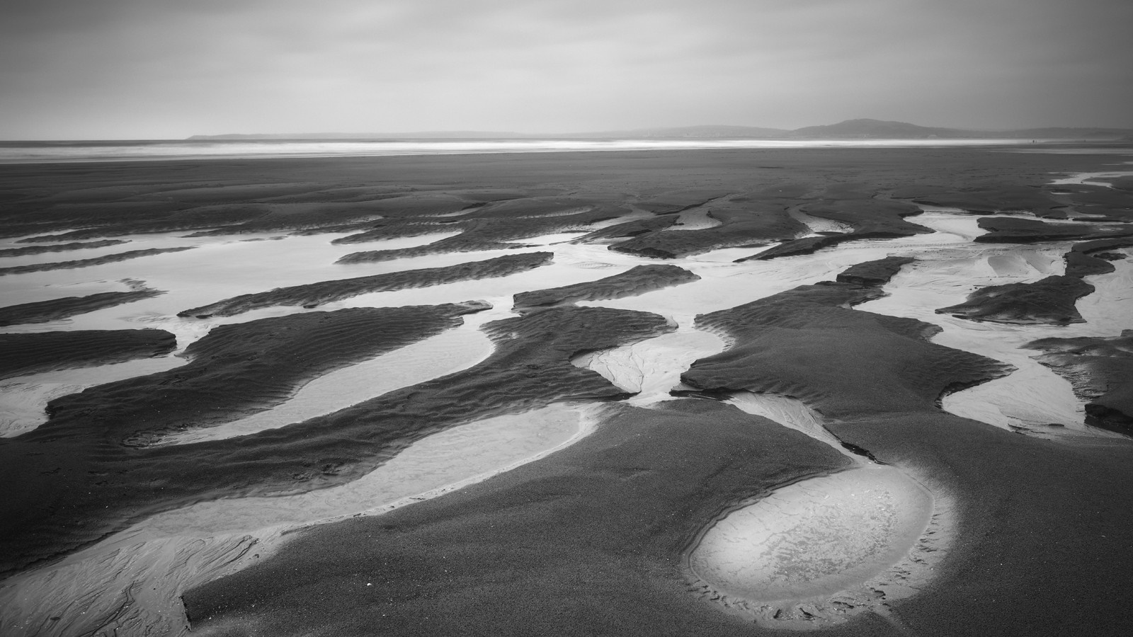 Monochrome beach with sand patterns and ocean horizon HD Wallpaper