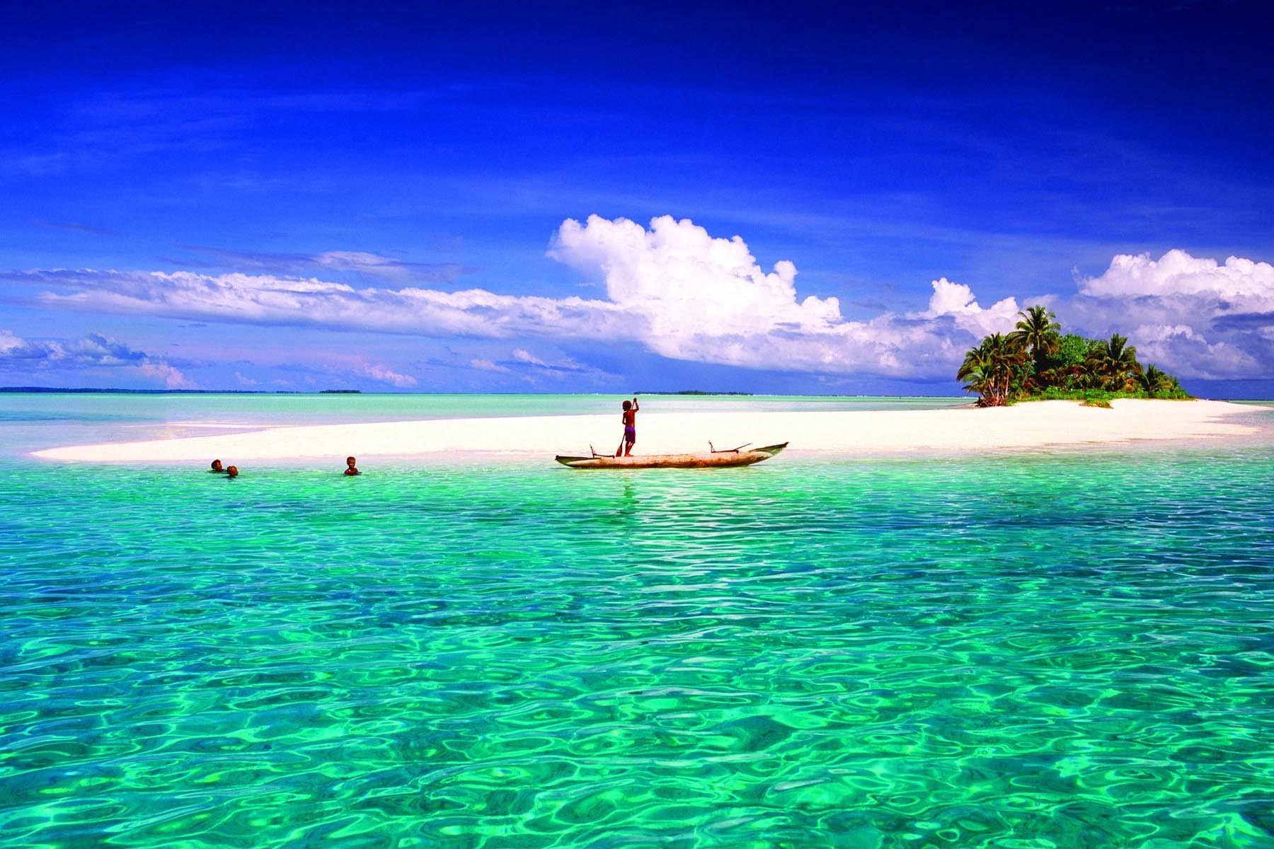 Tropical island with people swimming and a person in a canoe HD Wallpaper