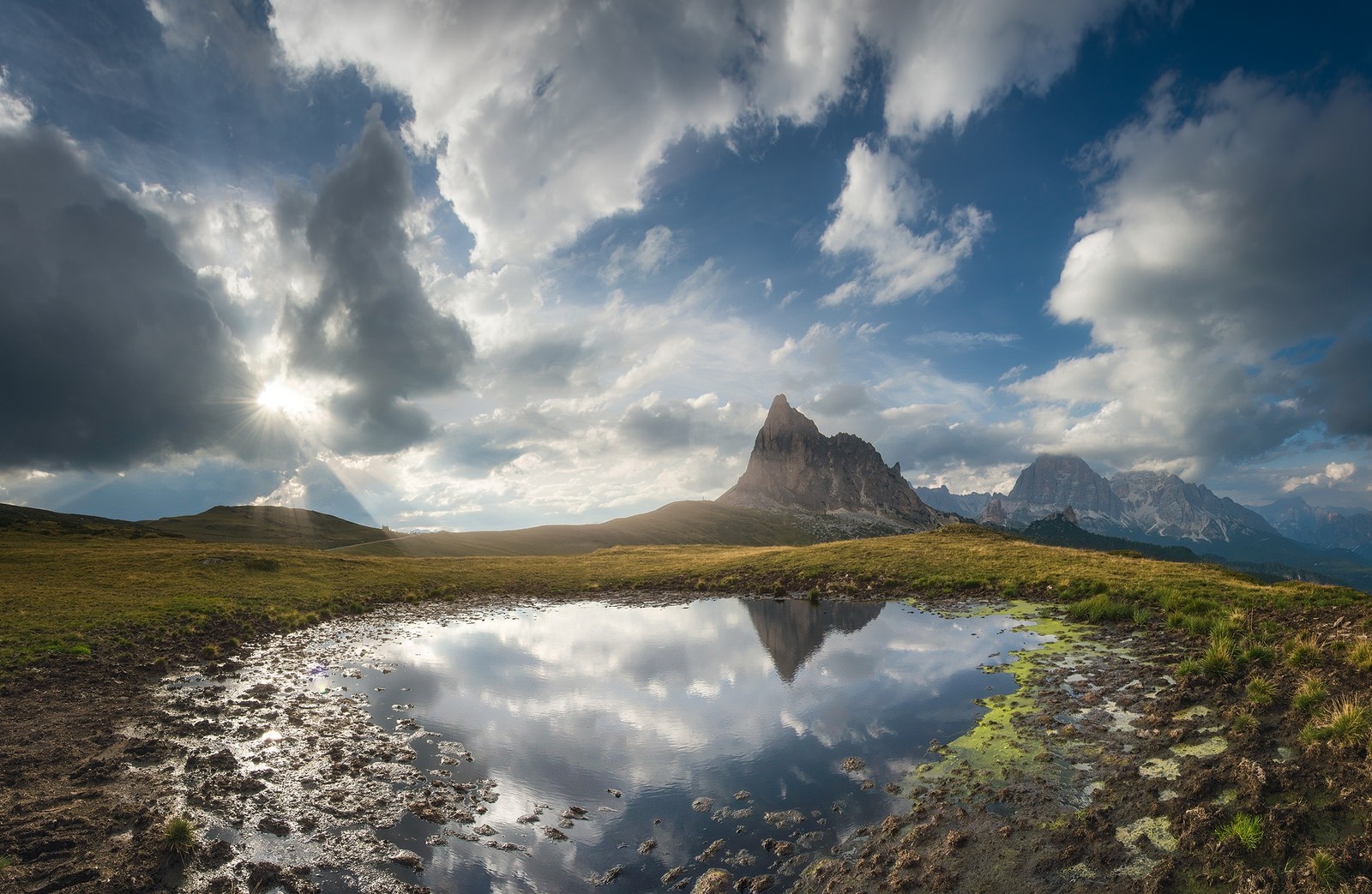 Mountain peak reflected in a puddle under a cloudy sky HD Wallpaper