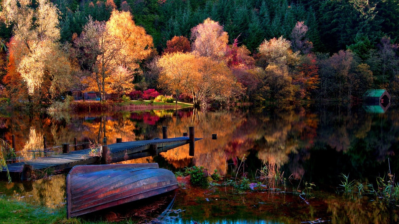 Autumn forest reflected in a lake with a boat and dock HD Wallpaper