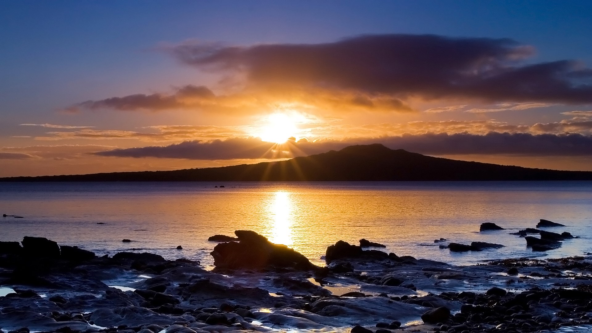 Sunset over the ocean with a volcanic island silhouette HD Wallpaper