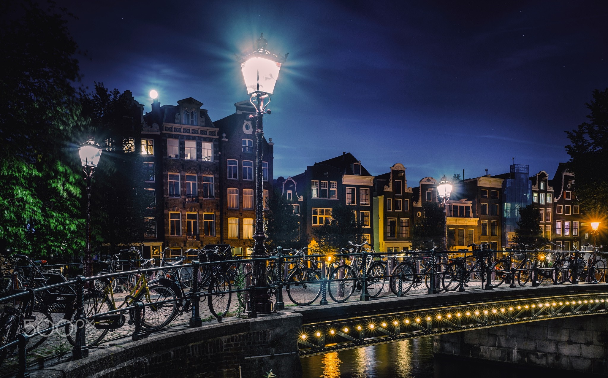 Amsterdam canal bridge at night with bicycles and buildings HD Wallpaper