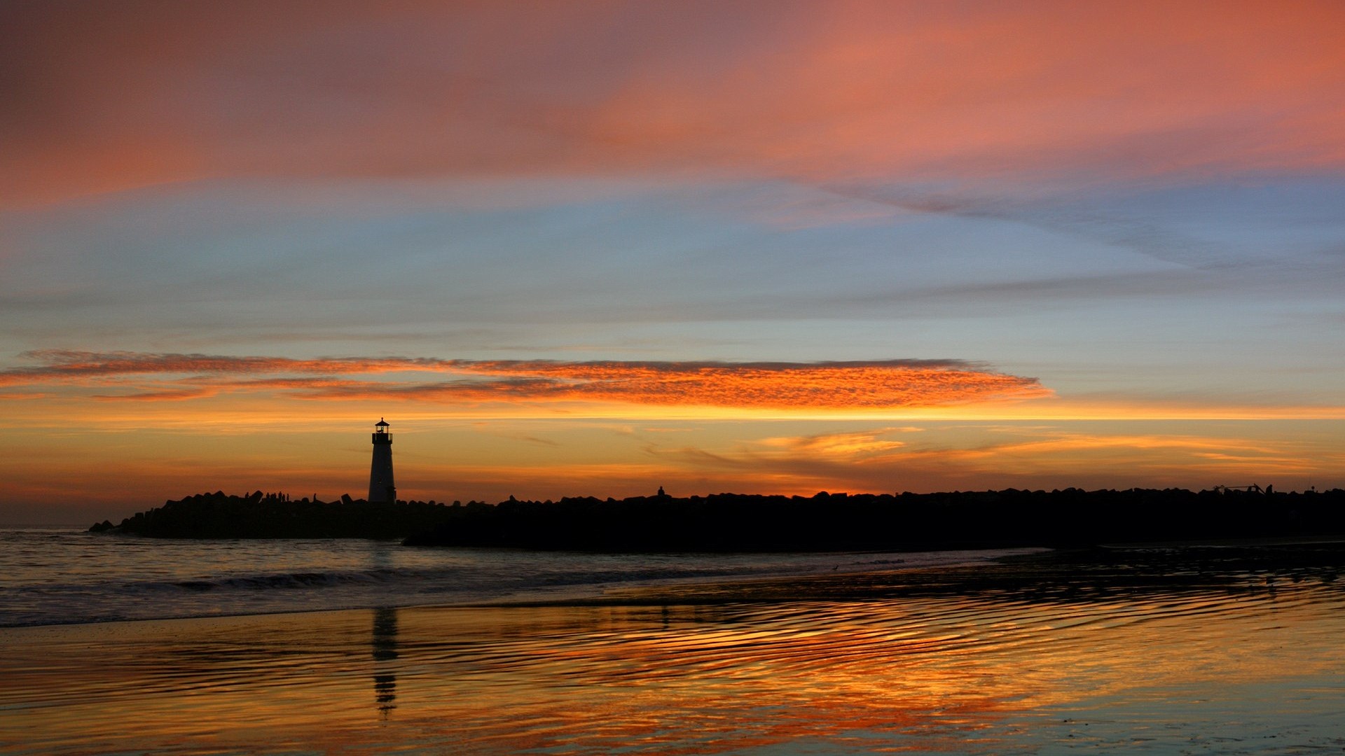 Lighthouse silhouetted against a colorful sunset over the ocean HD Wallpaper