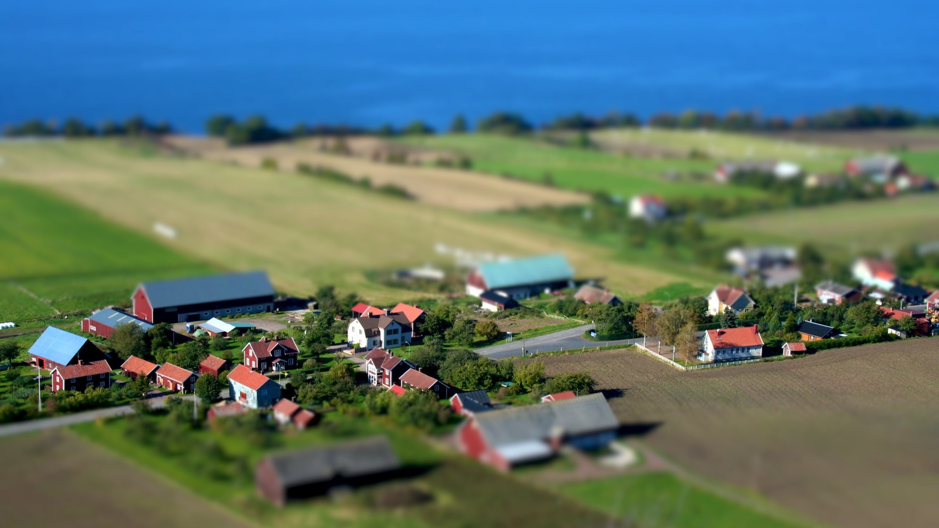 Tilt-shift aerial view of a rural village with farms and fields HD Wallpaper