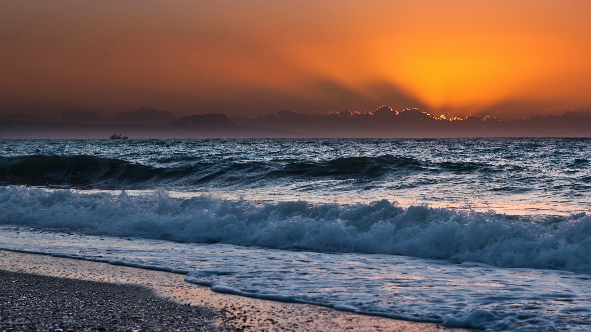 Sunset over the ocean with waves crashing on the shore HD Wallpaper