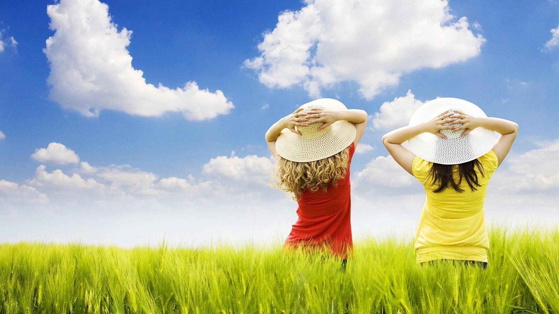 Two women in hats in a grassy field under a blue sky HD Wallpaper