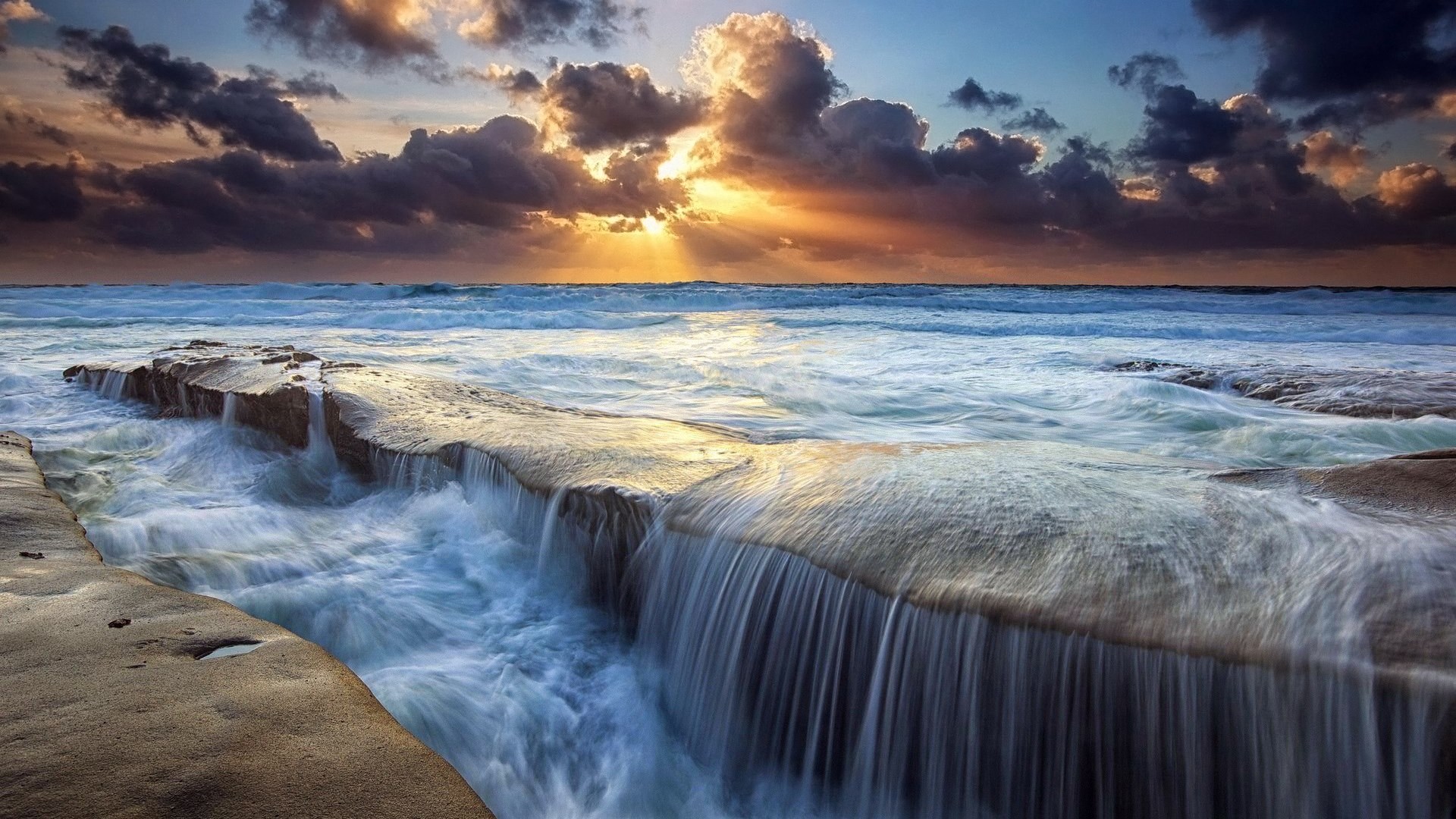 Ocean waves crashing over rocks at sunset HD Wallpaper