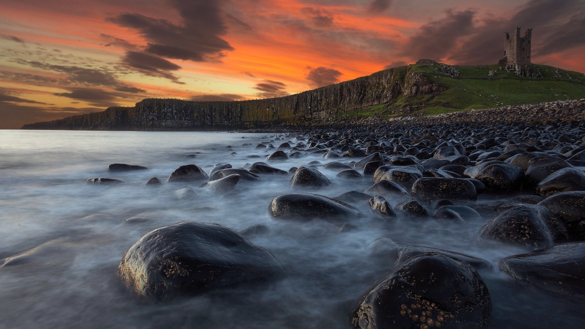 Castle ruins on a cliff overlooking a rocky shore at sunset HD Wallpaper