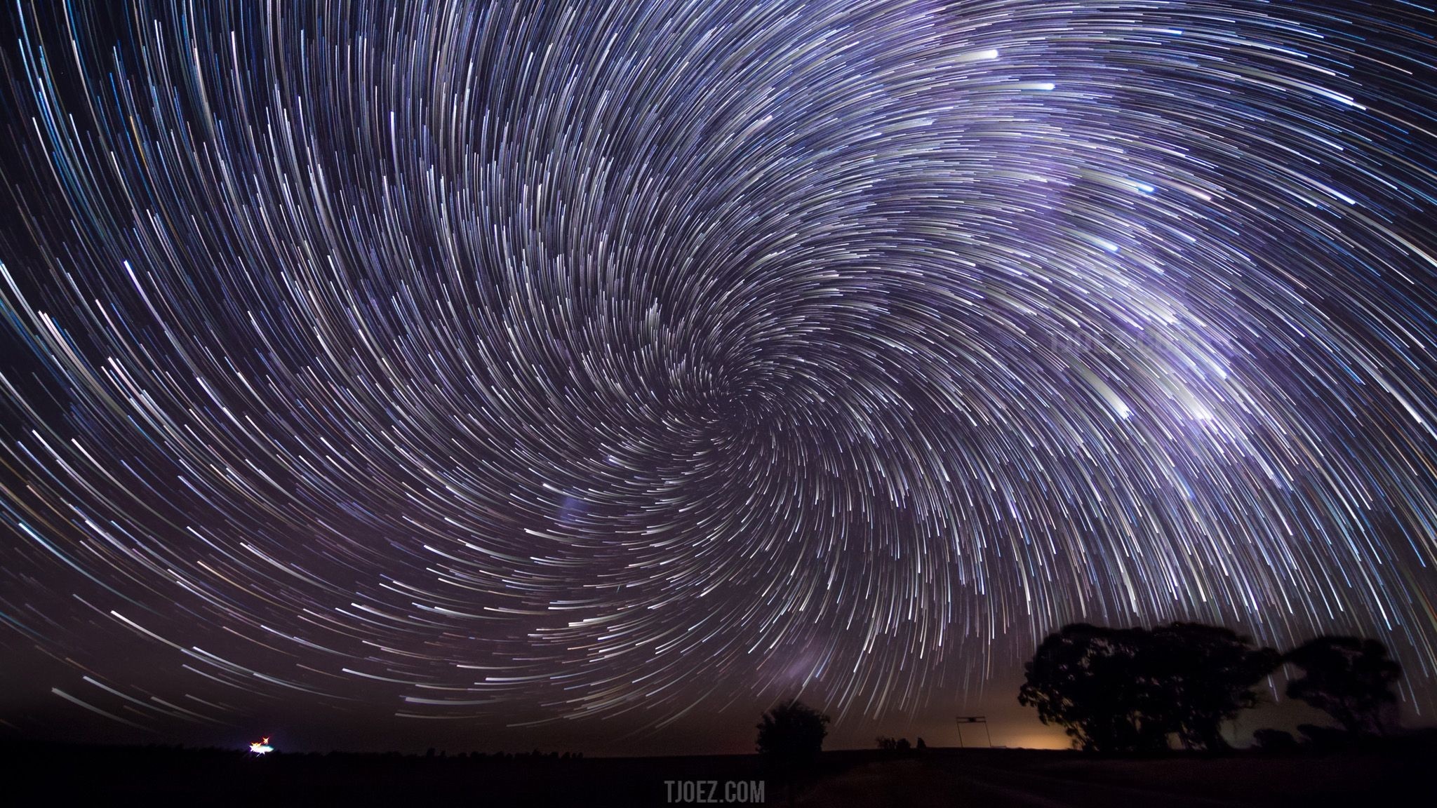 Star trails forming a spiral over a dark landscape HD Wallpaper