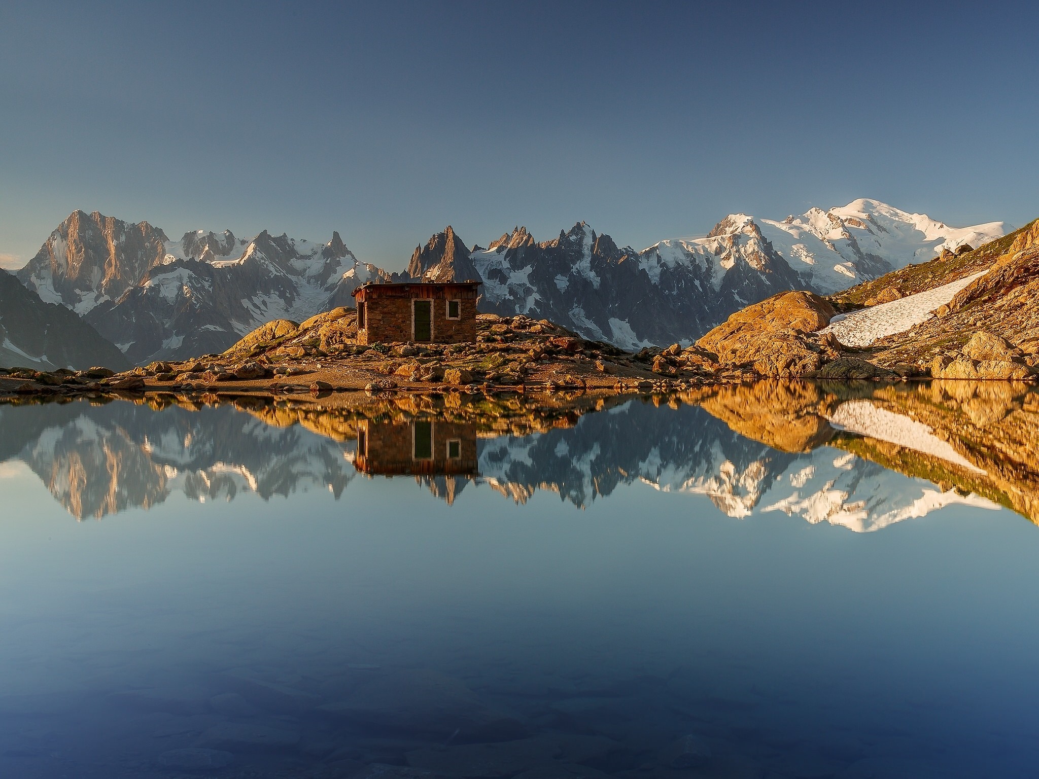 Mountain cabin reflected in a calm lake at sunrise HD Wallpaper