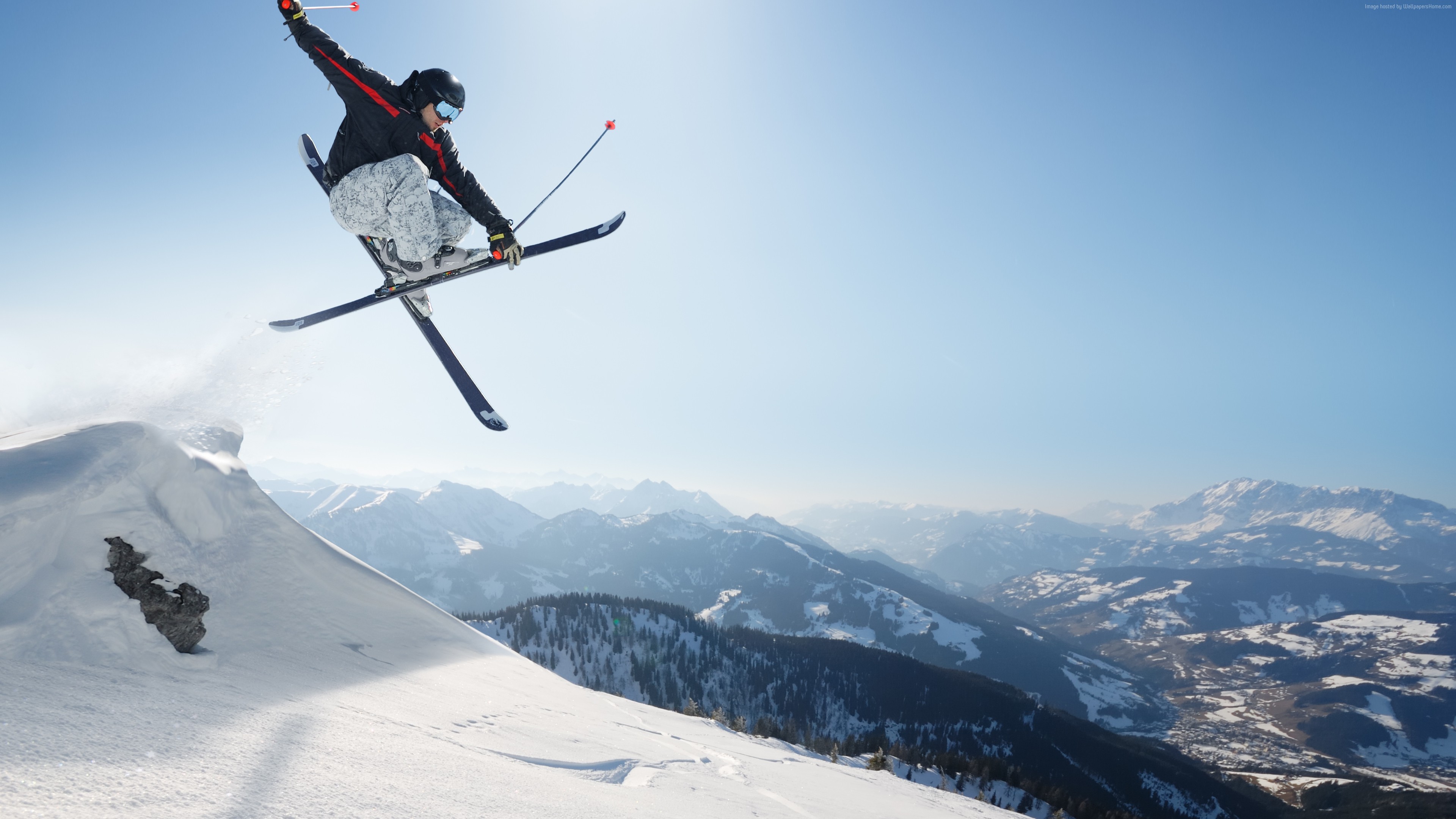 Skier performing a jump over a snowy mountain landscape HD Wallpaper