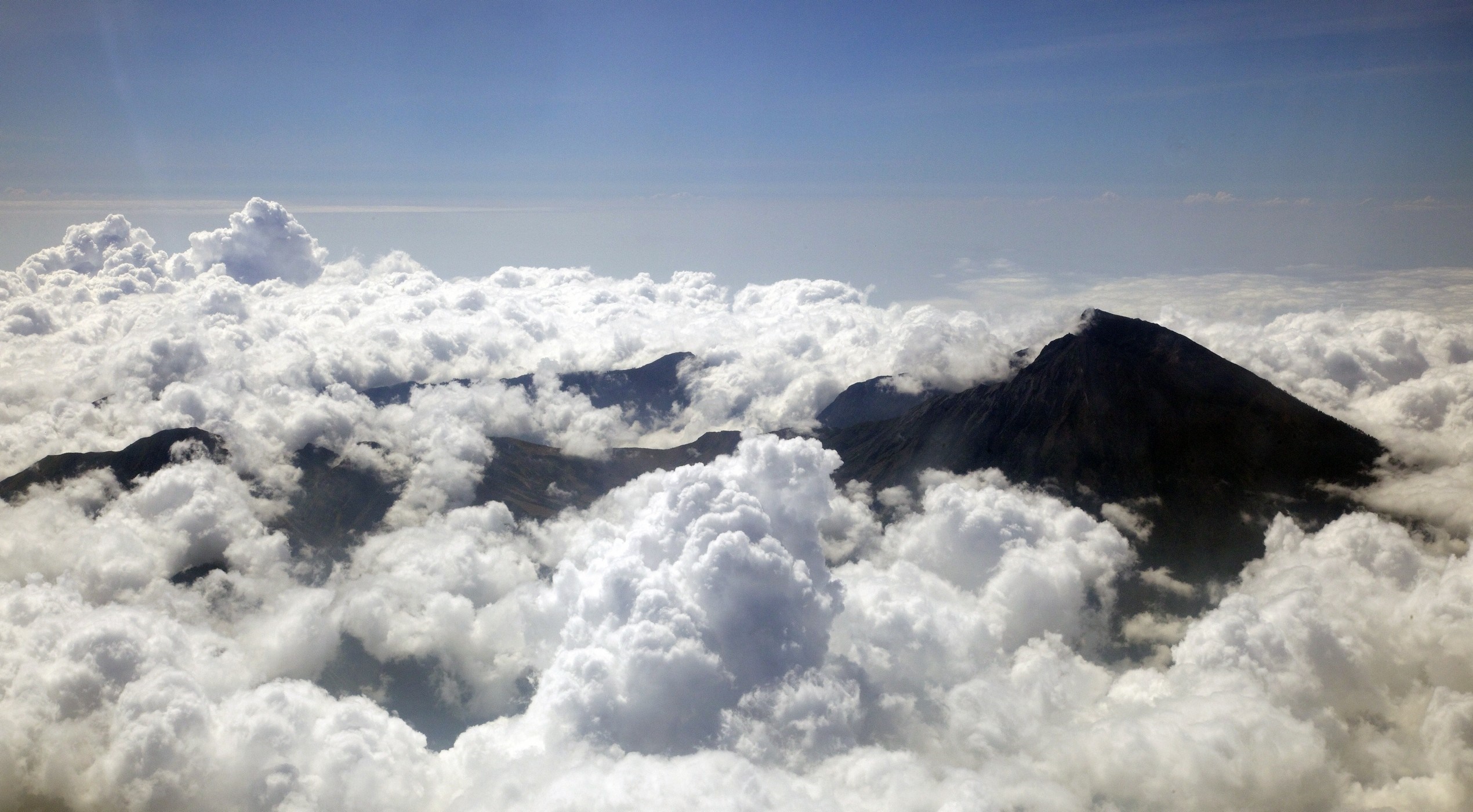 Mountain peaks emerging from clouds under a blue sky HD Wallpaper