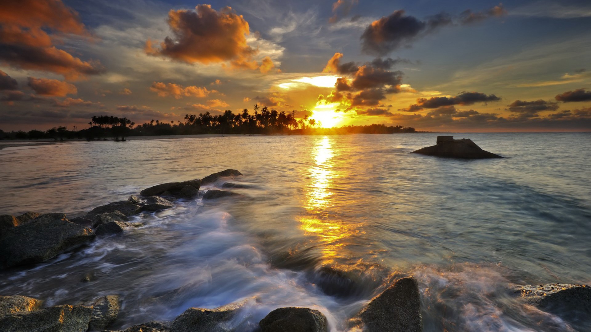 Sunset over the ocean with rocks and palm trees HD Wallpaper