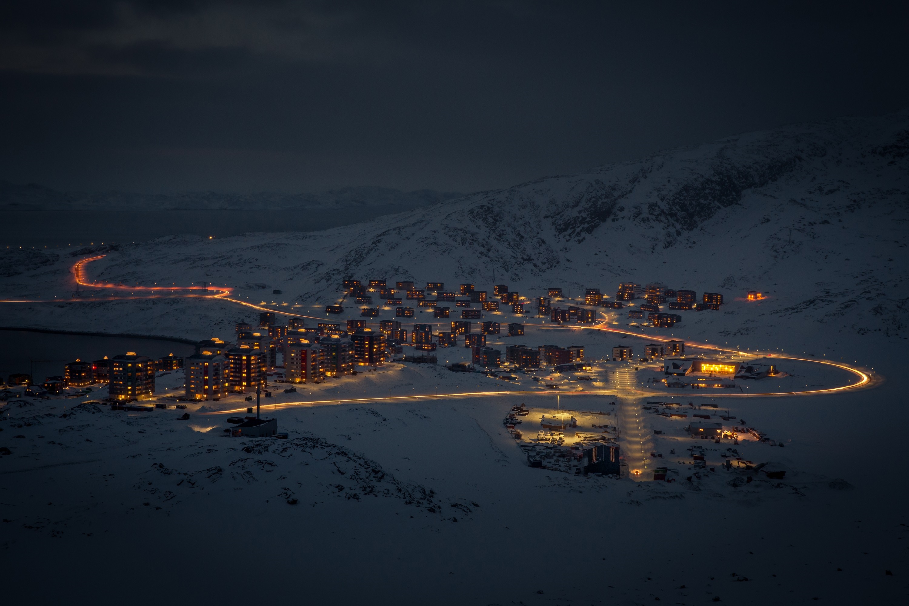Snowy town at night with illuminated buildings and car lights HD Wallpaper