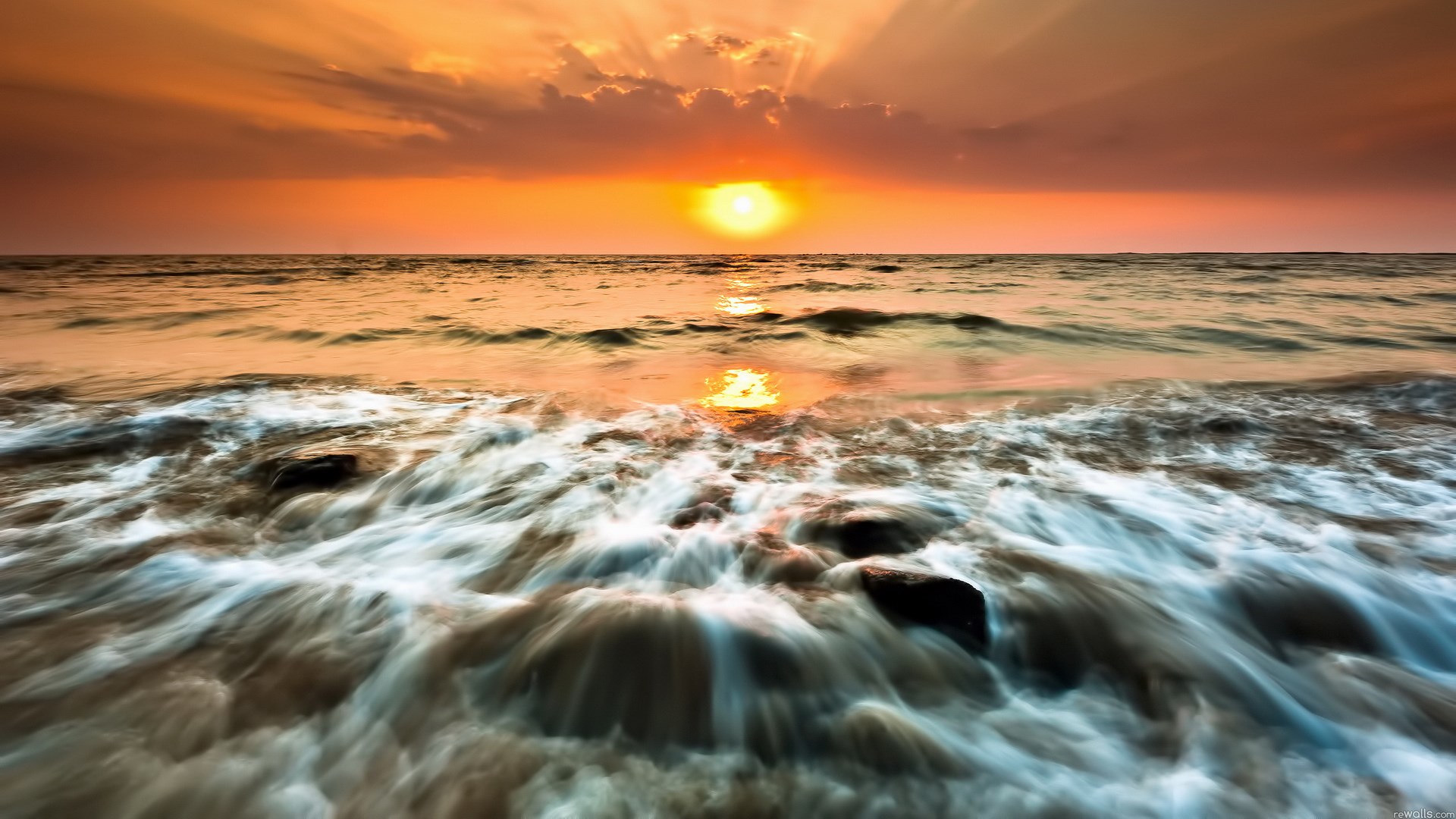 Sunset over the ocean with waves crashing on rocks HD Wallpaper